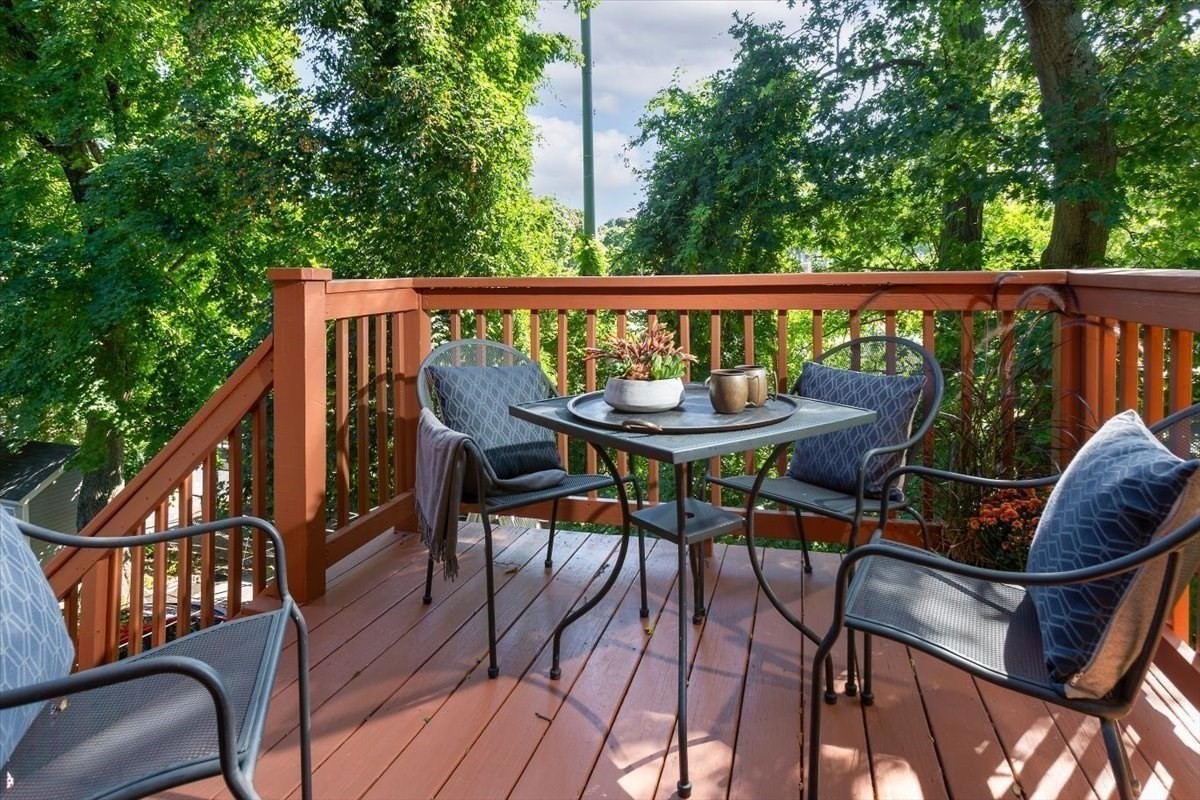 Furnished wooden deck with cushioned chairs and a small table, surrounded by leafy trees.