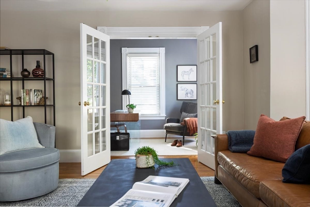 Living room with a brown leather sofa, opening through French doors to a sitting room and desk.