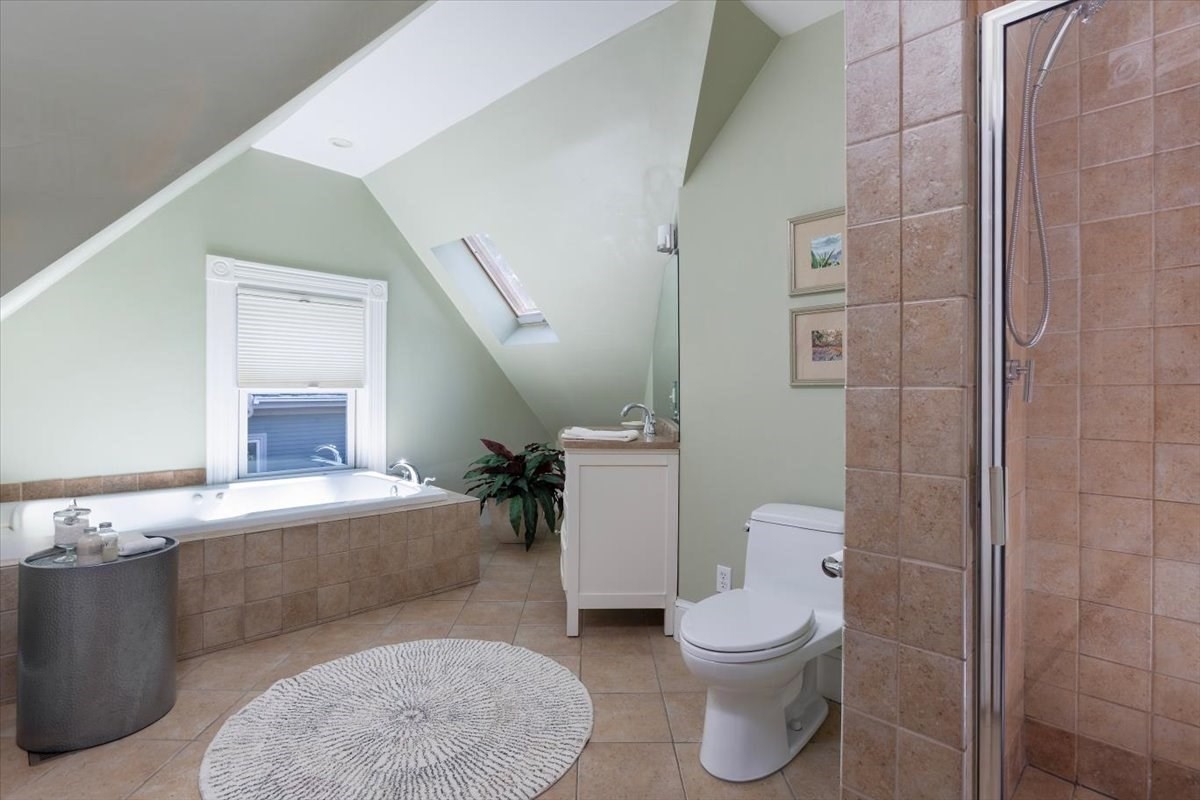 Attic bathroom with a soaking tub, skylight, tiled shower, and sloped ceiling.