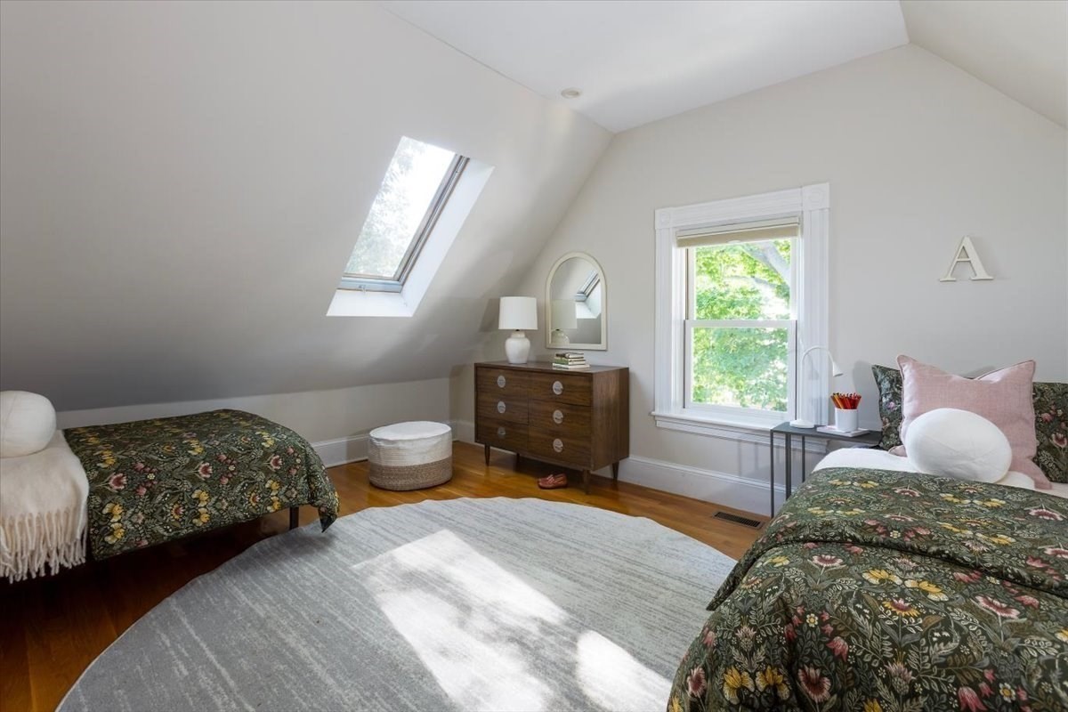 Bedroom with two floral-covered beds, a skylight, and a wooden dresser.