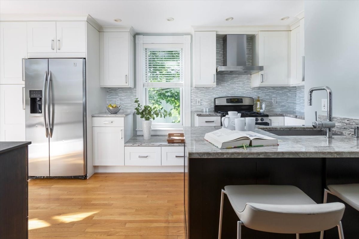 Bright kitchen with white cabinets, stainless steel appliances, and a dark island with seating.