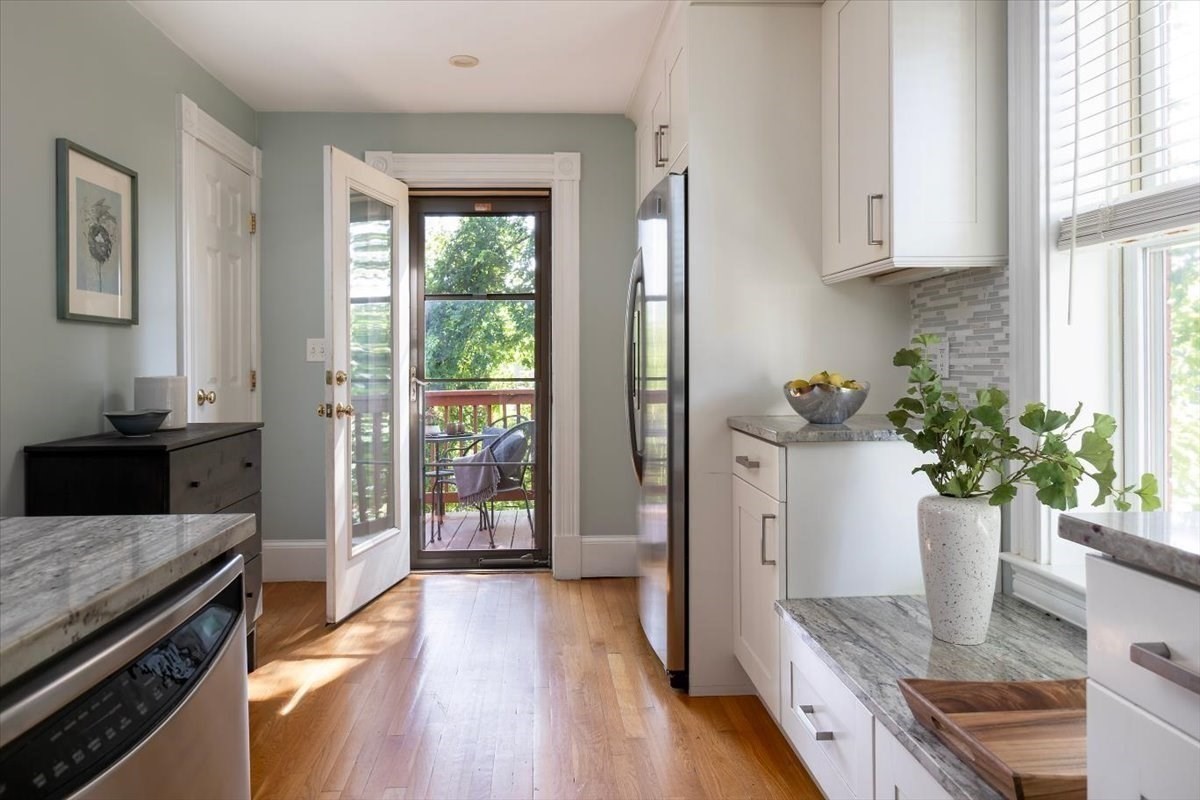 Bright white kitchen with stone counters and an open door leading to a leafy deck.