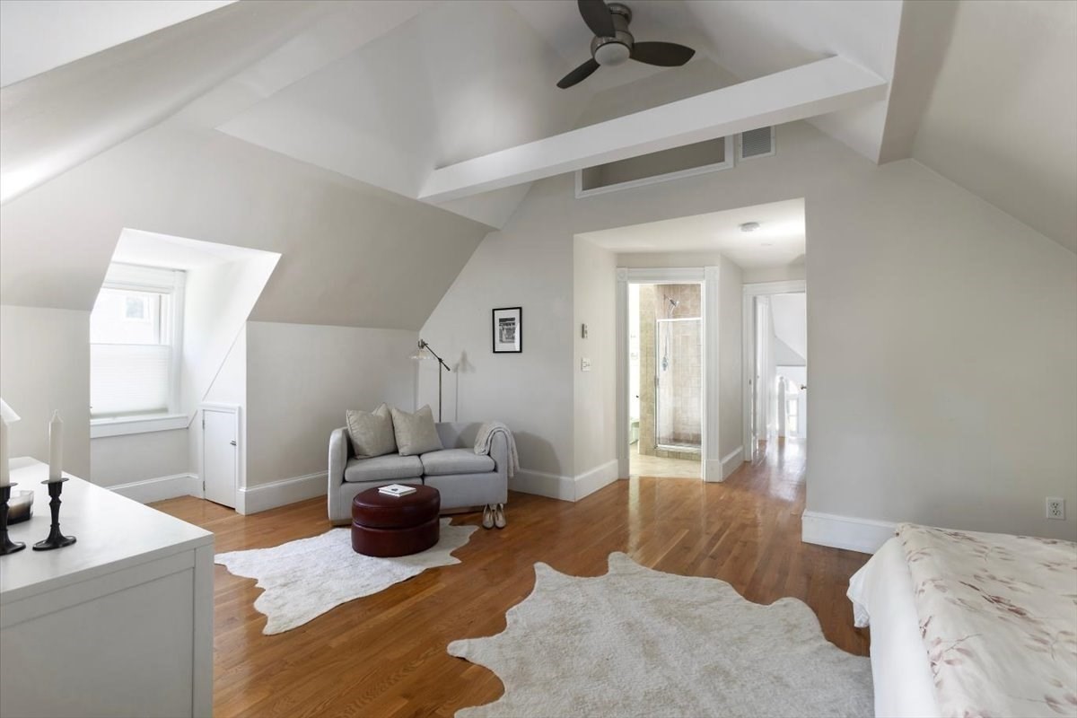 Attic bedroom with a vaulted ceiling, hardwood floors, and a gray sofa sitting area.