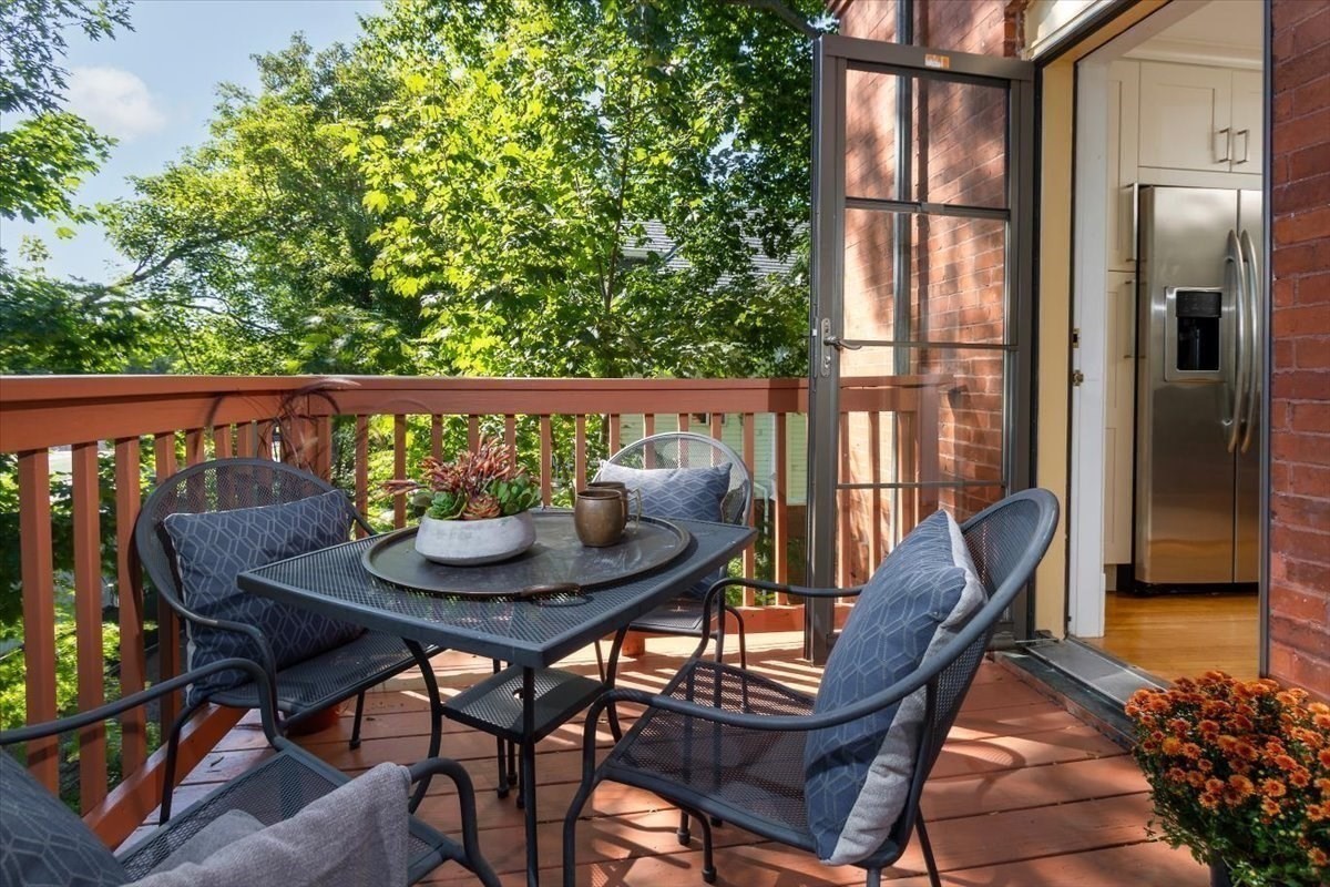 Furnished deck with a metal dining set, potted plants, and leafy trees beside an open kitchen door.