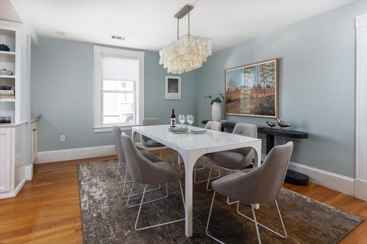 Dining room with a white table, gray chairs, patterned rug, and statement chandelier.