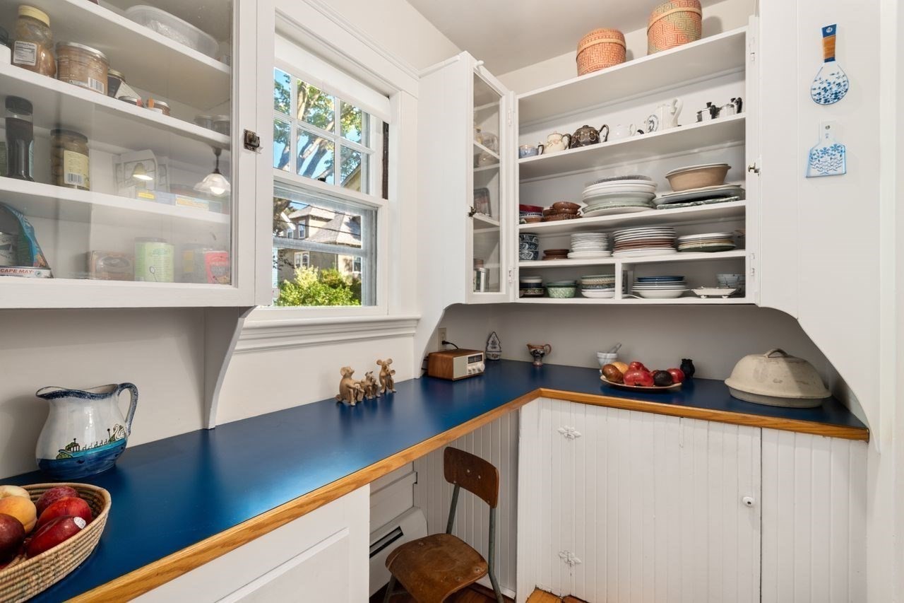 Kitchen with white dish-filled cabinets, blue countertops, and a window overlooking greenery.