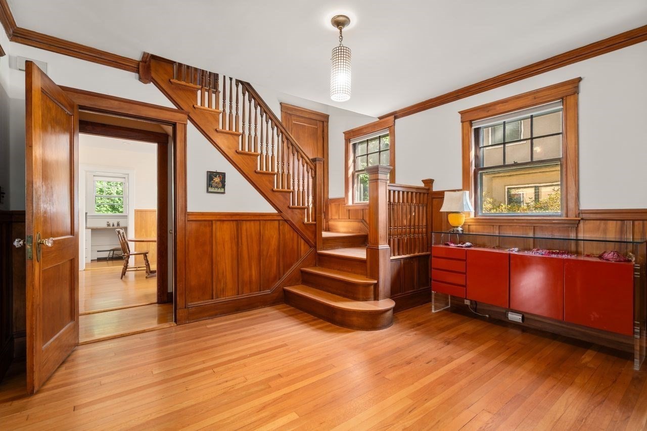 Wood-paneled entry hall with a curved staircase, polished hardwood floors, and a red display cabinet.