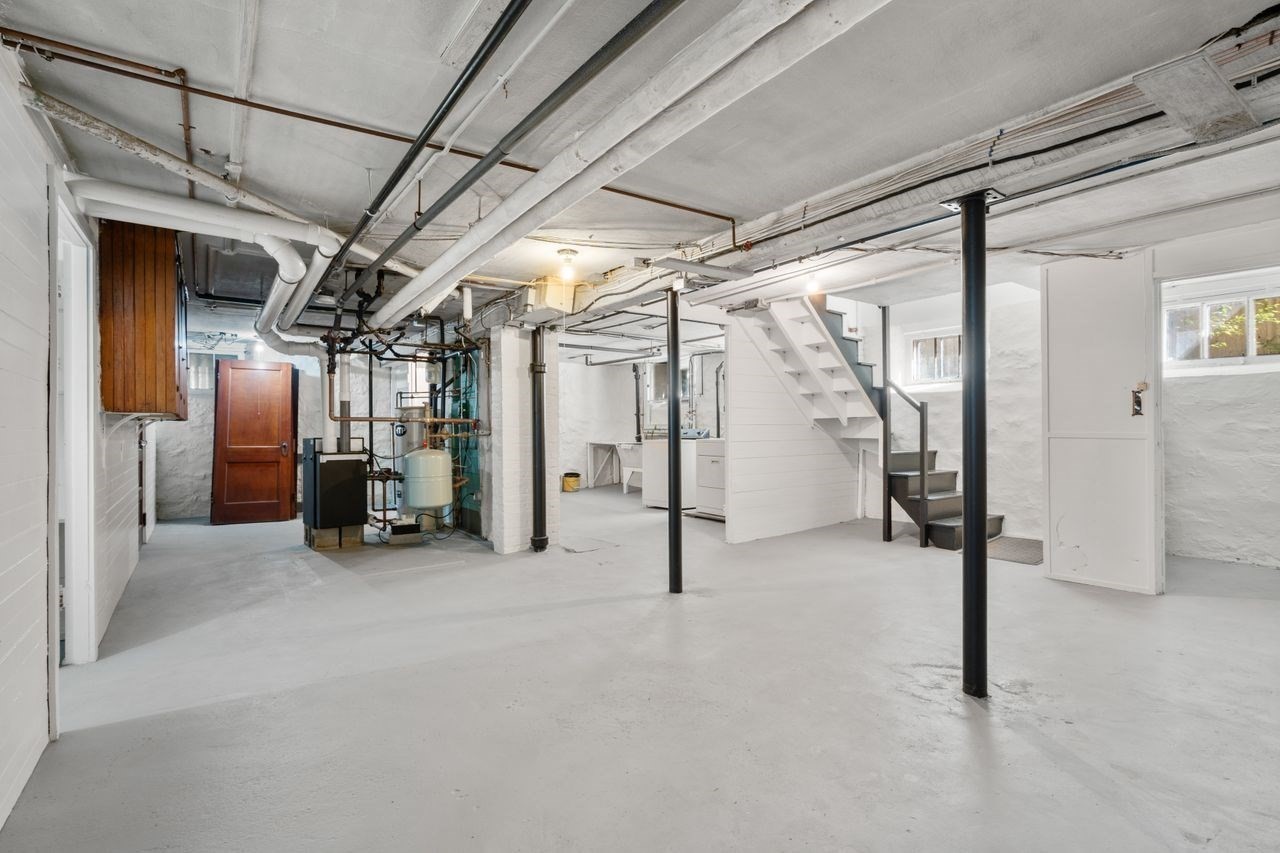 Unfinished basement with exposed pipes, mechanical equipment, and stairs.