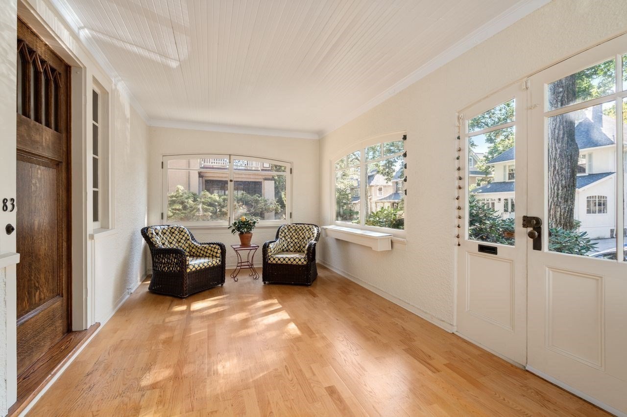 Sunroom with hardwood floors, large windows, and two patterned wicker chairs.