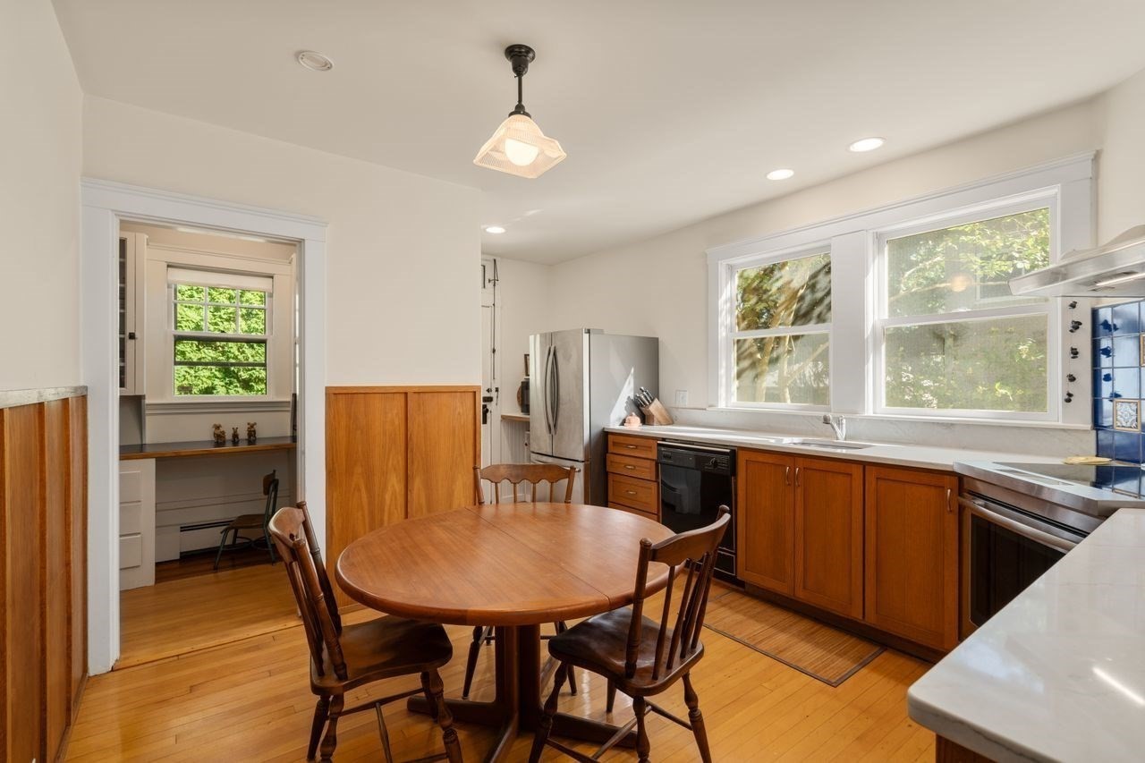 Kitchen with warm wood cabinets, a round dining table, and large windows overlooking greenery.