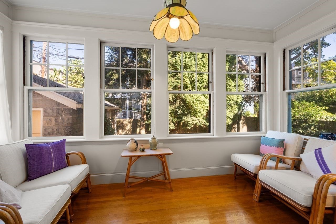 Sunroom with tall windows, white seating, hardwood floors, and a stained-glass pendant light.