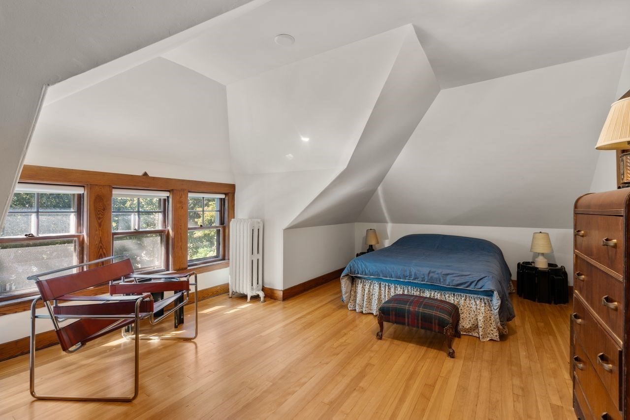 Attic bedroom with a bed beneath a sharply sloped ceiling and wood-trimmed windows.