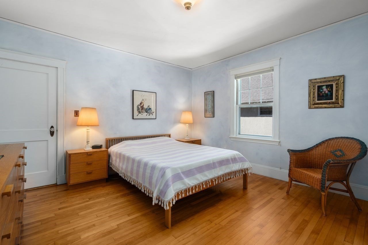 Bedroom with a striped bedspread, hardwood floors, pale blue walls, and a wicker chair.