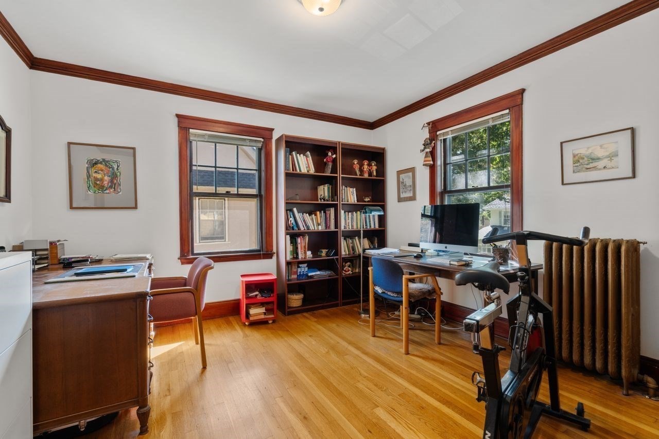 Home office with built-in bookshelves, two desks, and an exercise bike by the window.