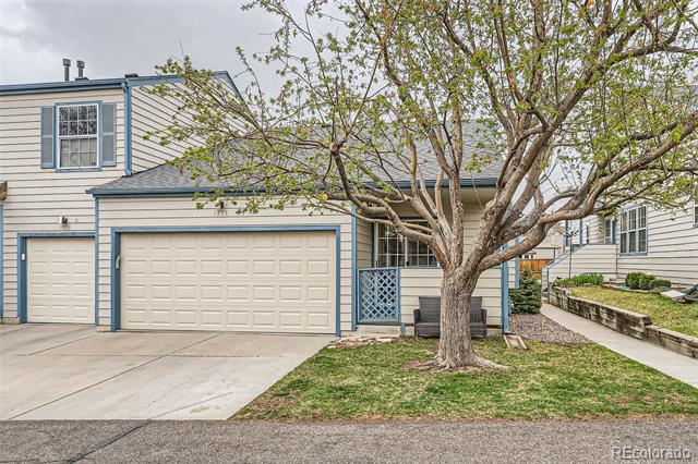 Two-story townhouse with blue trim, two garage doors, and a mature tree in the front yard.