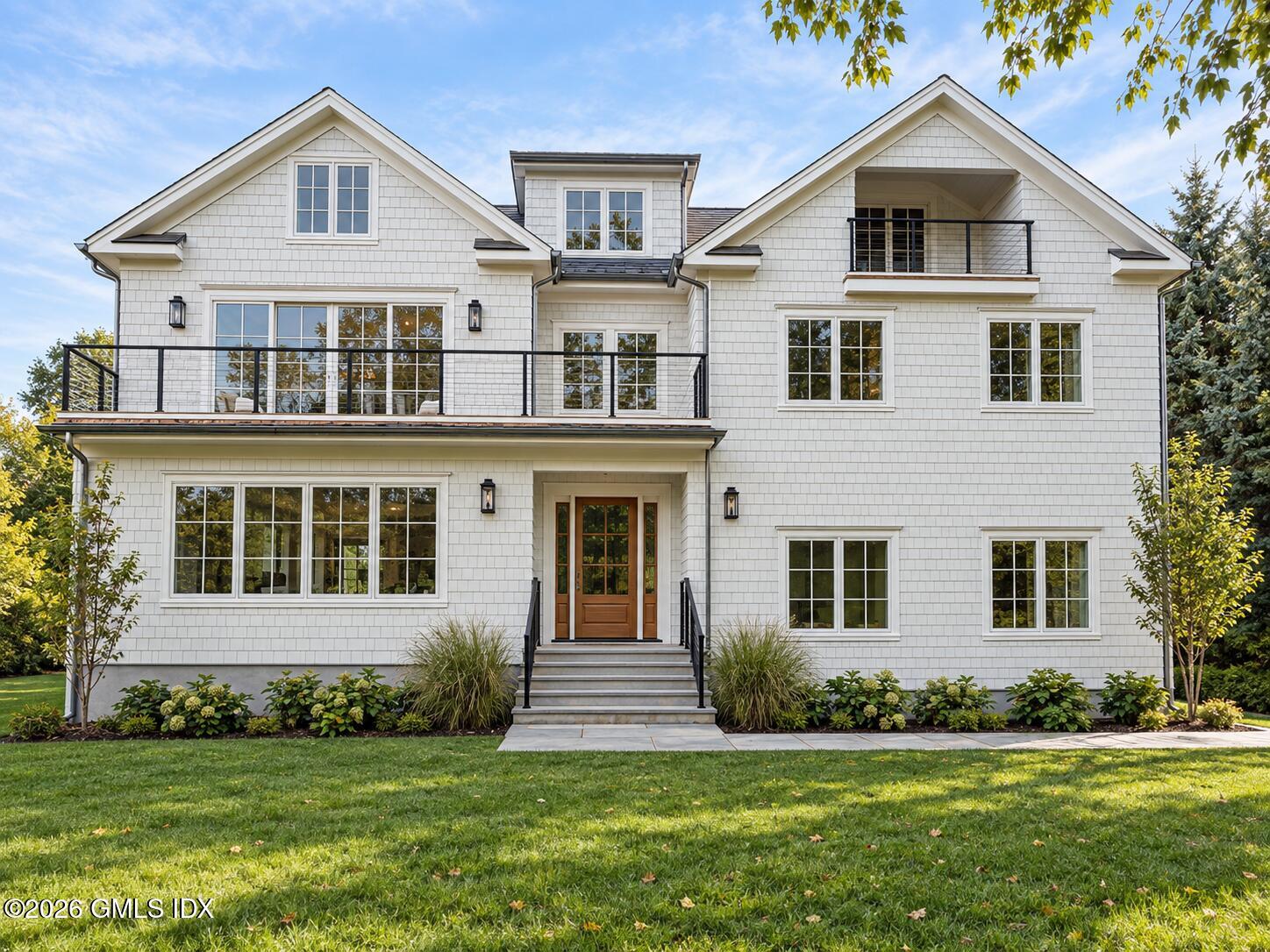 White shingle-style house with multiple gables, black balcony railings, and a central wood front door.