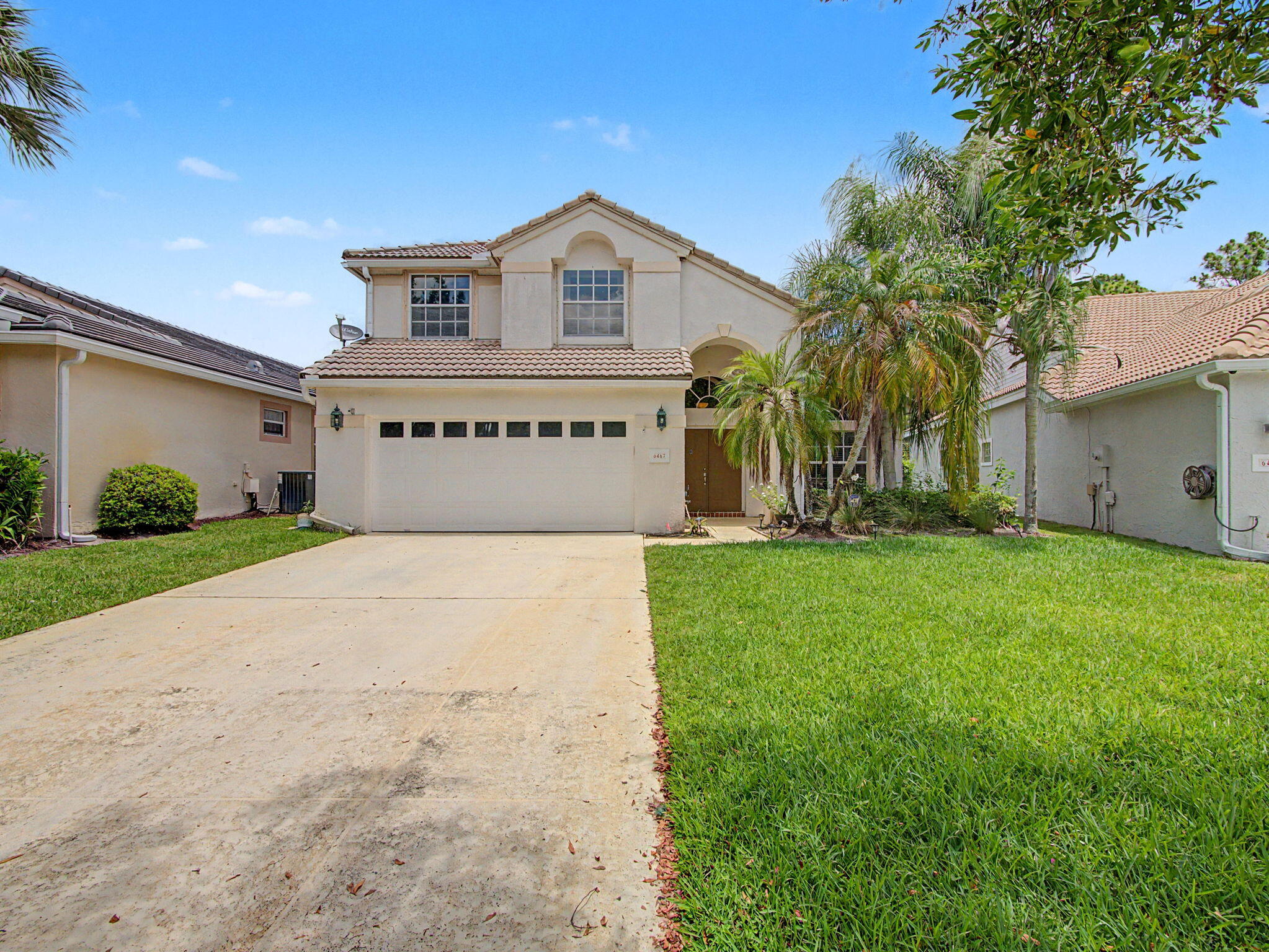 Two-story stucco home with a tiled roof, double garage, and palm-lined front yard.