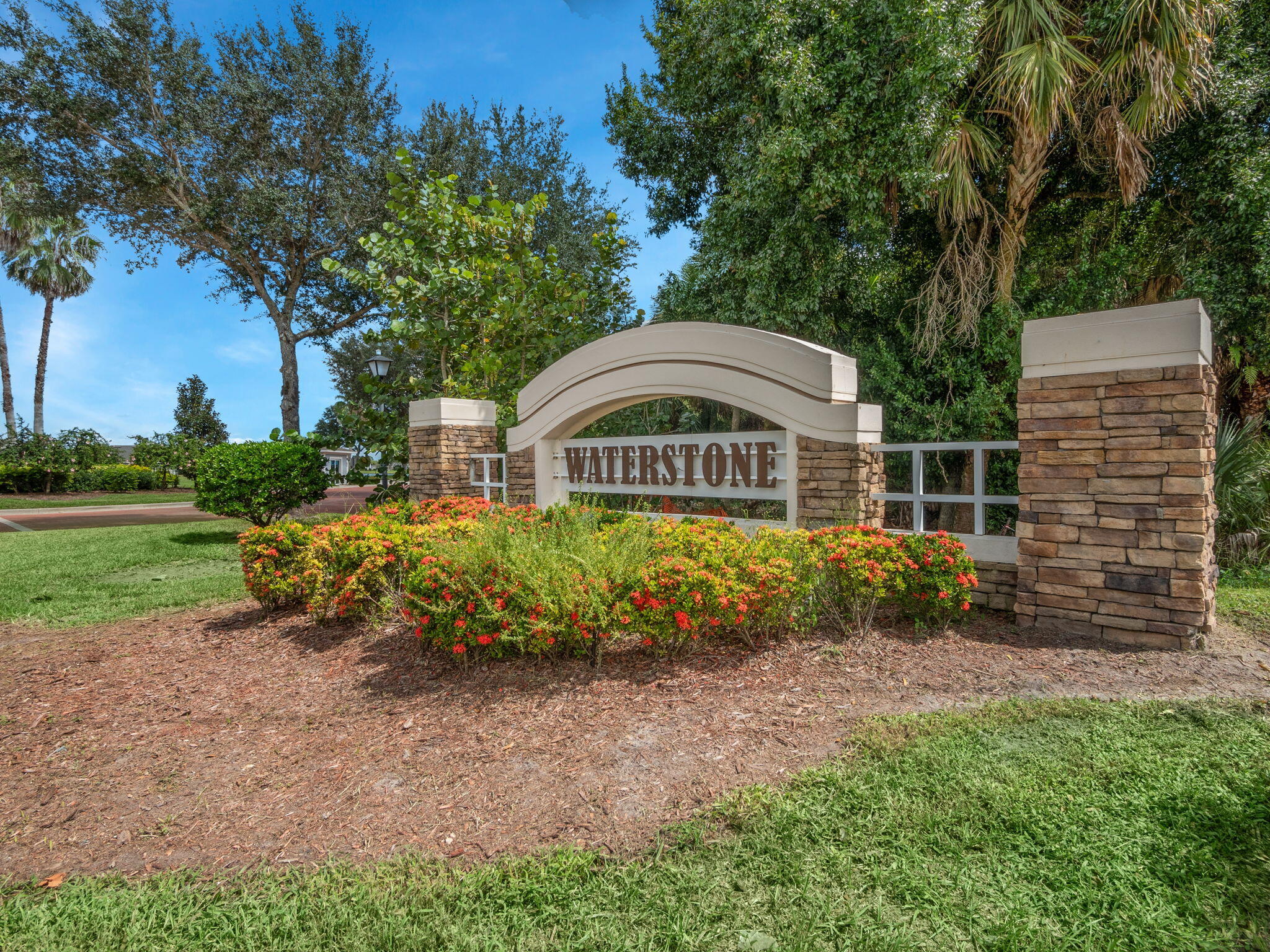 Waterstone community entrance sign framed by flowering hedges and stone pillars.