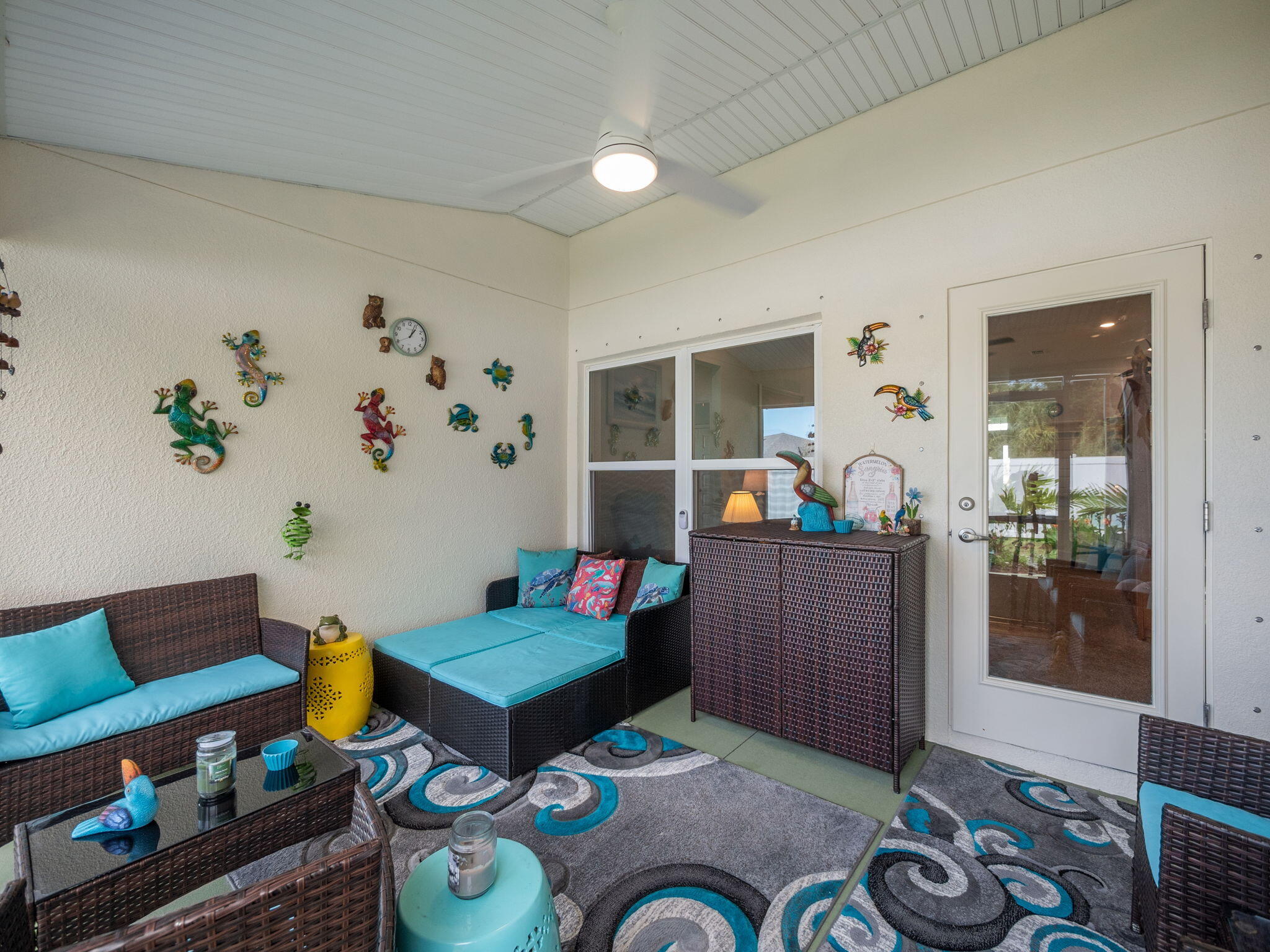 Covered patio with turquoise-cushioned wicker seating, colorful rugs, and playful wall decorations.