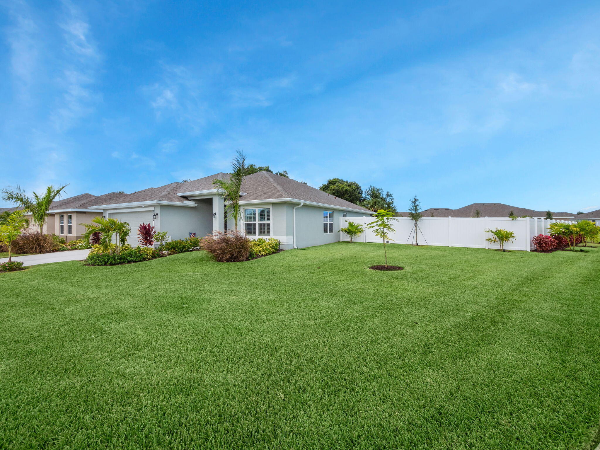 Single-story gray home beside a broad lawn, landscaped beds, and white privacy fencing.