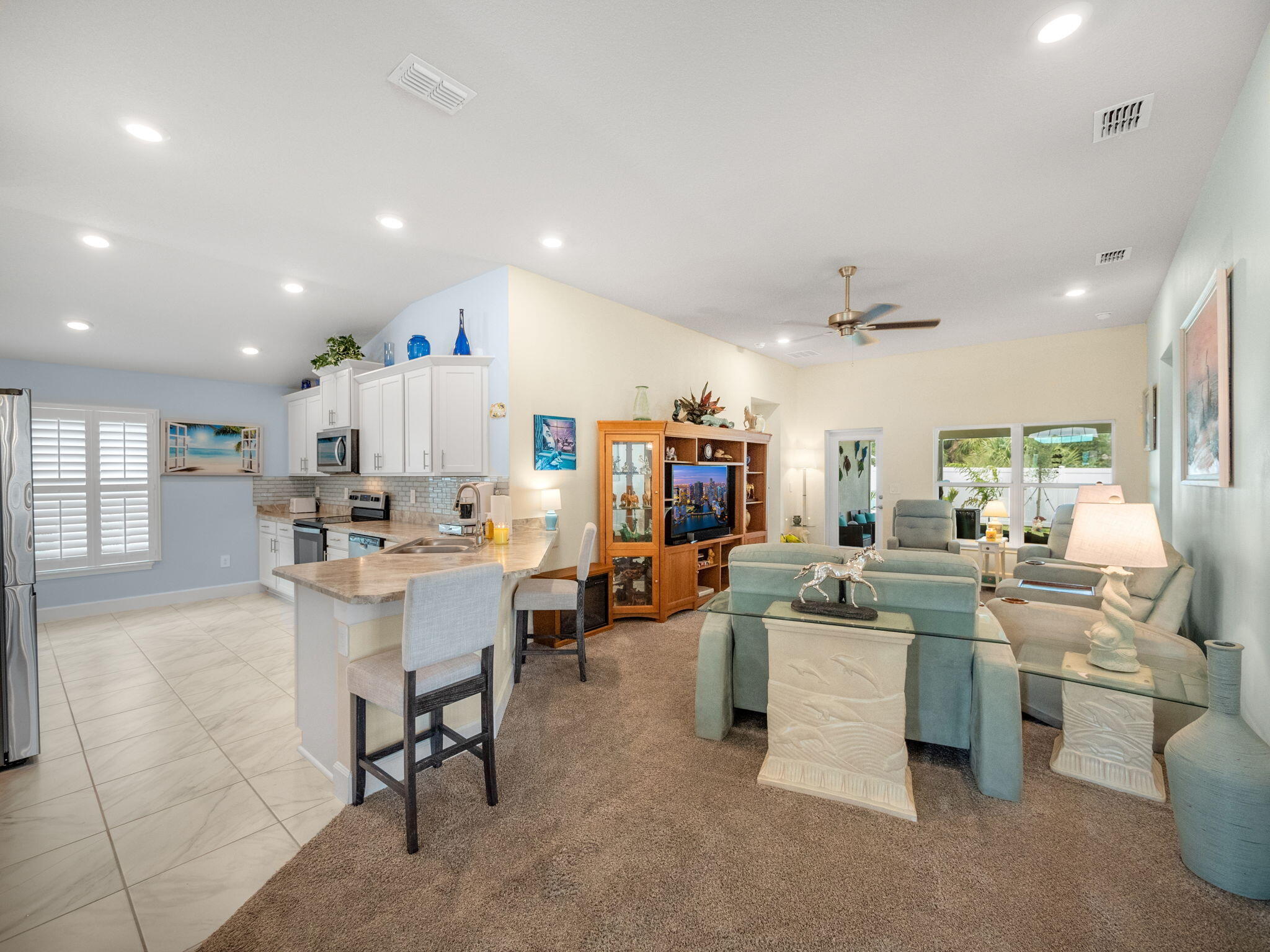 Open-plan living room and kitchen with a breakfast bar, white cabinets, and teal seating.