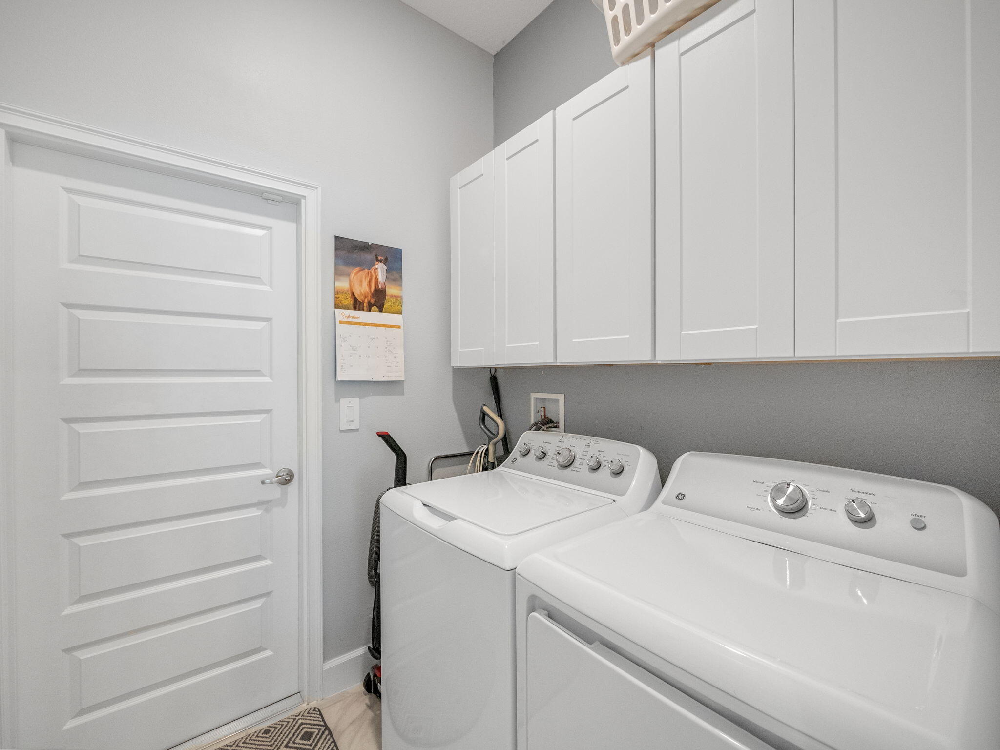 Laundry room with white washer and dryer beneath upper cabinets.