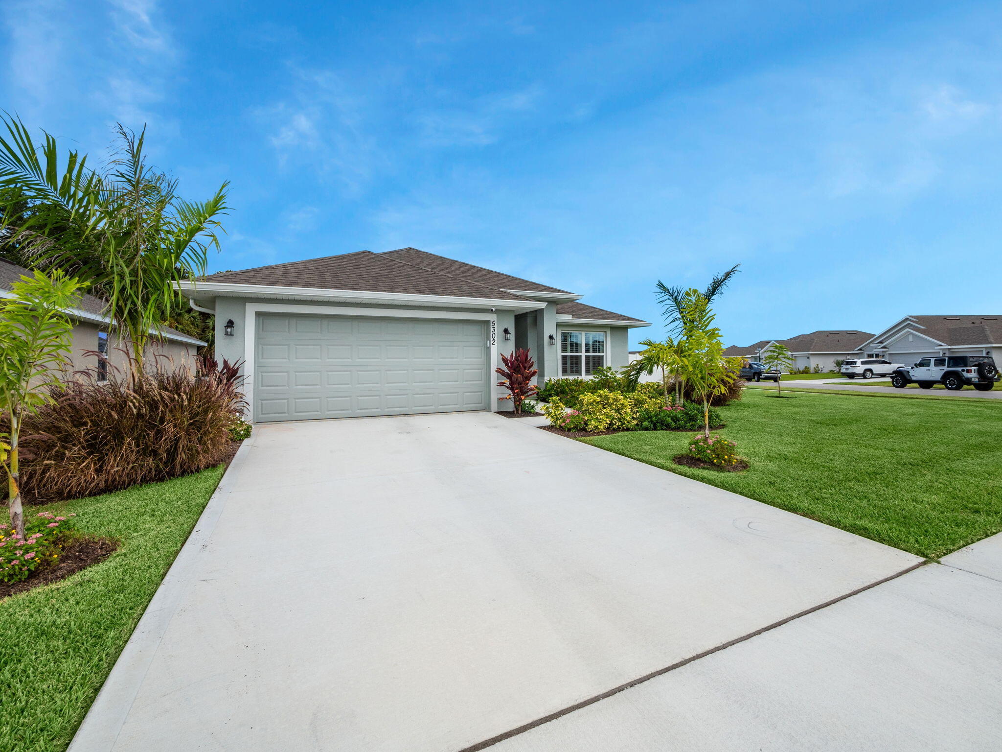 Single-story home with a wide garage, broad driveway, and tropical landscaping.