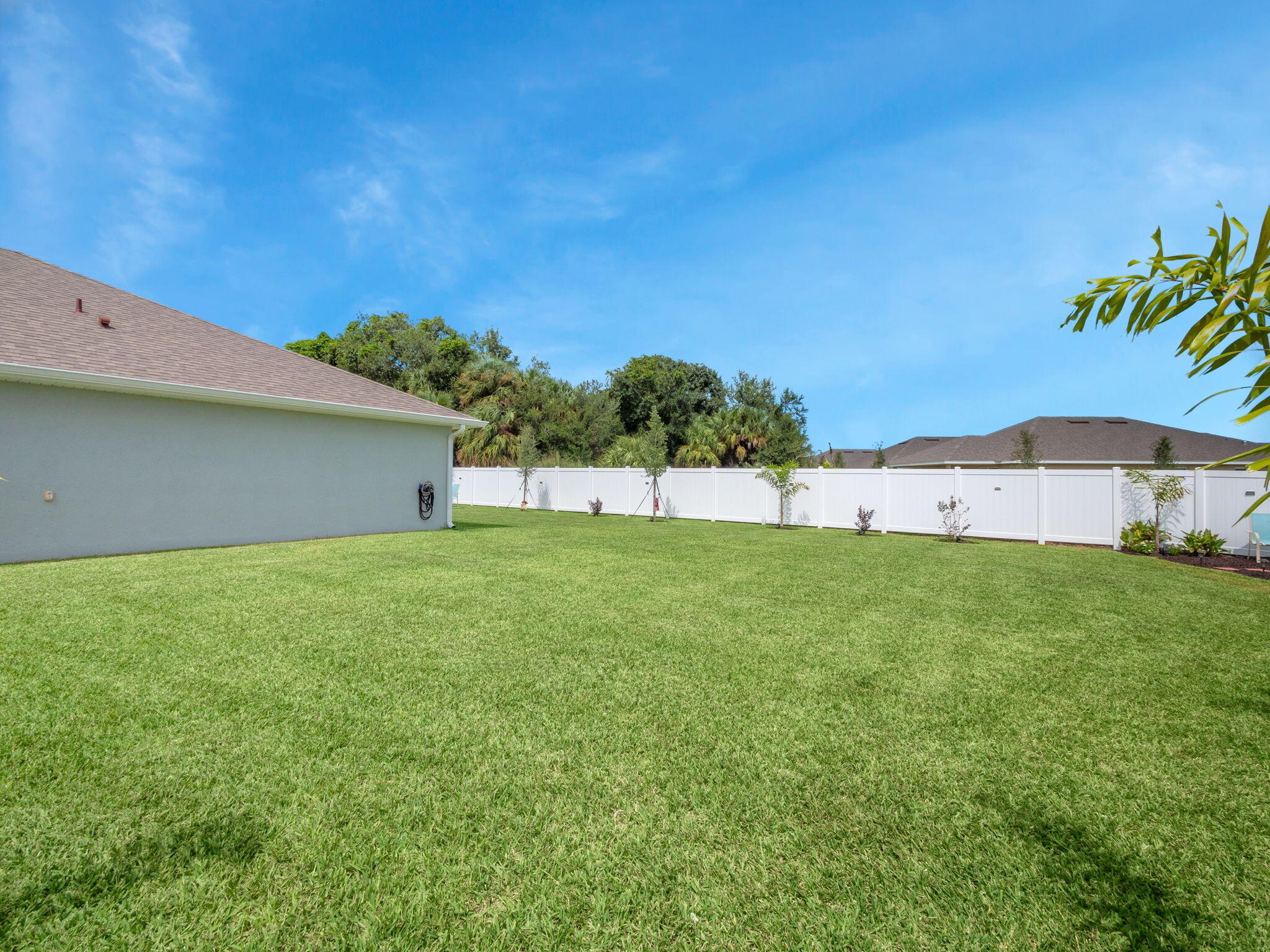Backyard with a broad green lawn and white privacy fence.