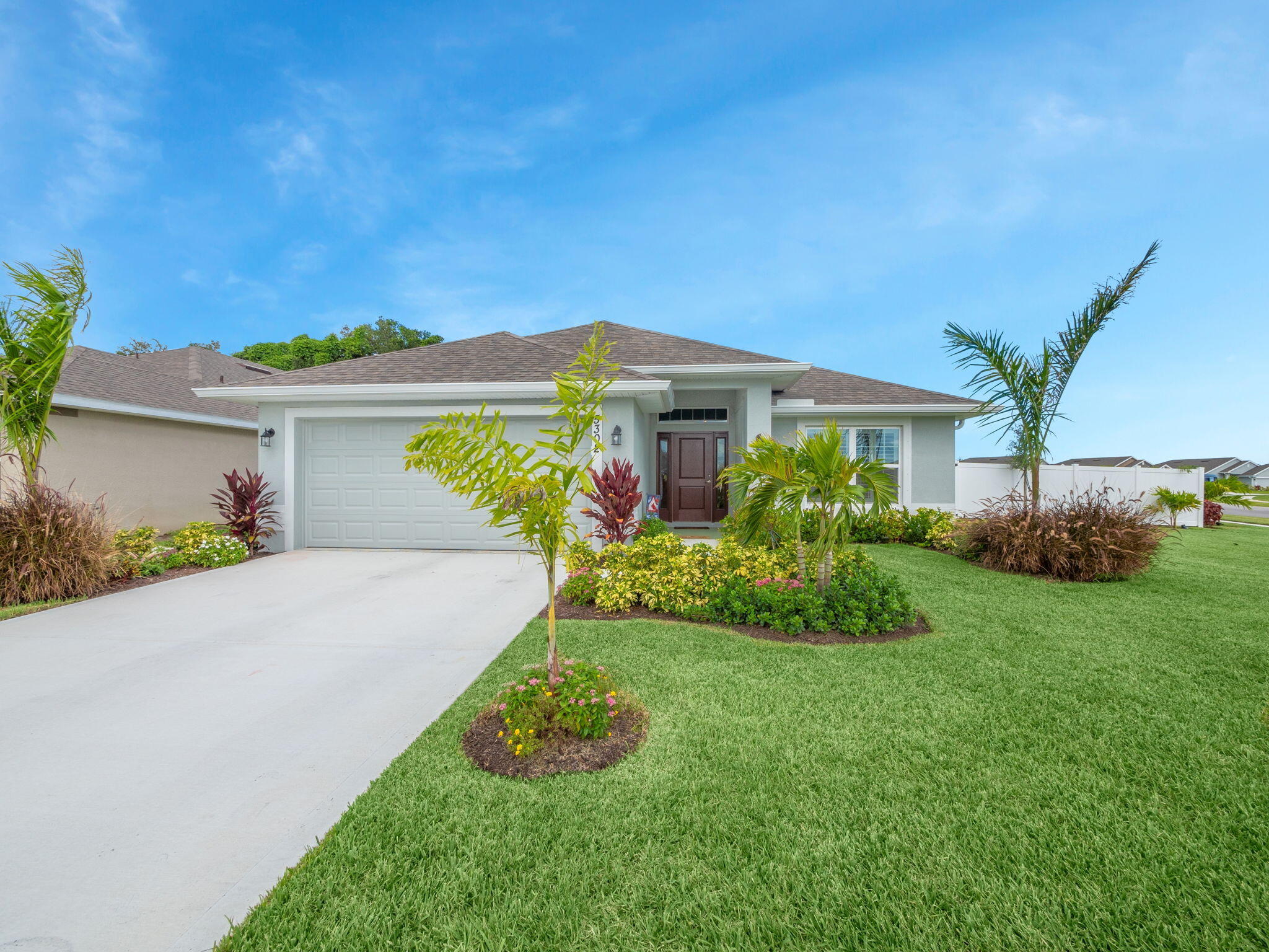 Single-story home with a two-car garage, palm landscaping, and a broad concrete driveway.