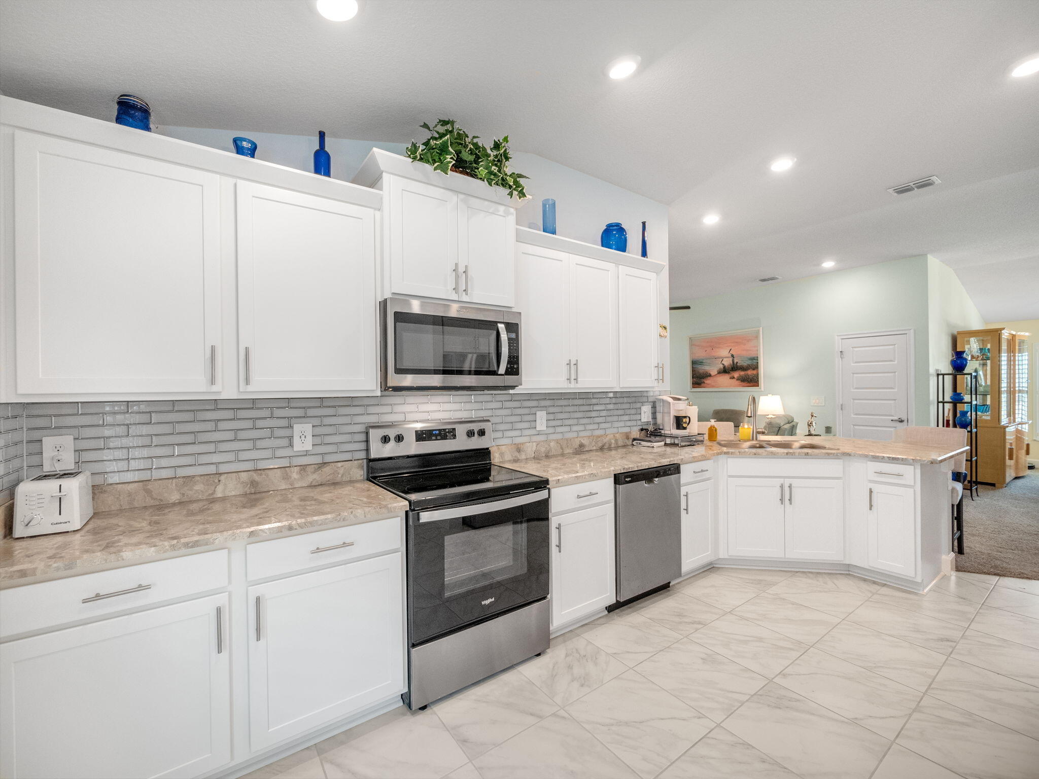 Kitchen with white shaker cabinets, gray tile backsplash, marble-look counters and stainless steel appliances.