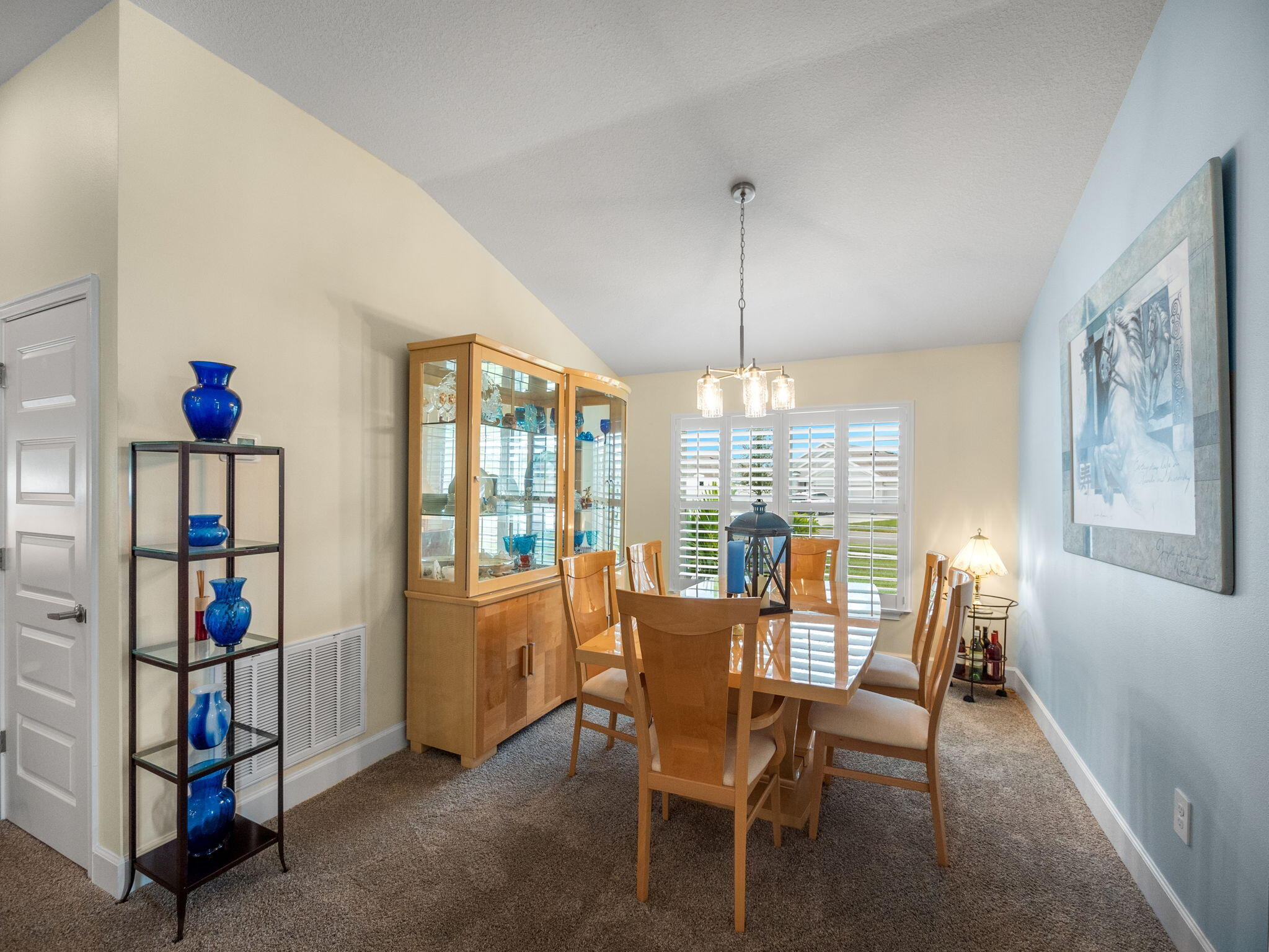 Furnished dining room with a wooden table, glass-front china cabinet, and plantation shutters.