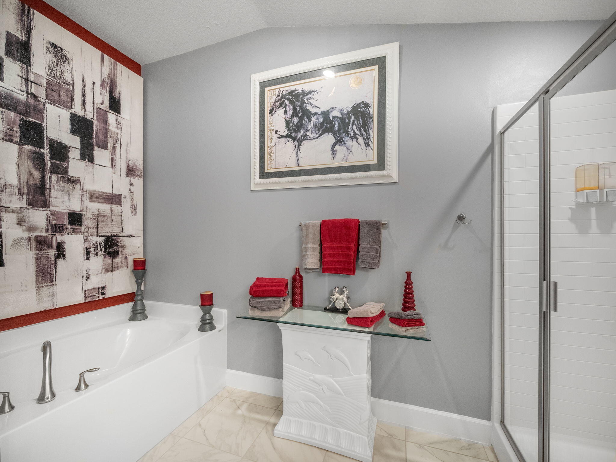 Bathroom with a white soaking tub, glass shower, and red towels against gray walls.