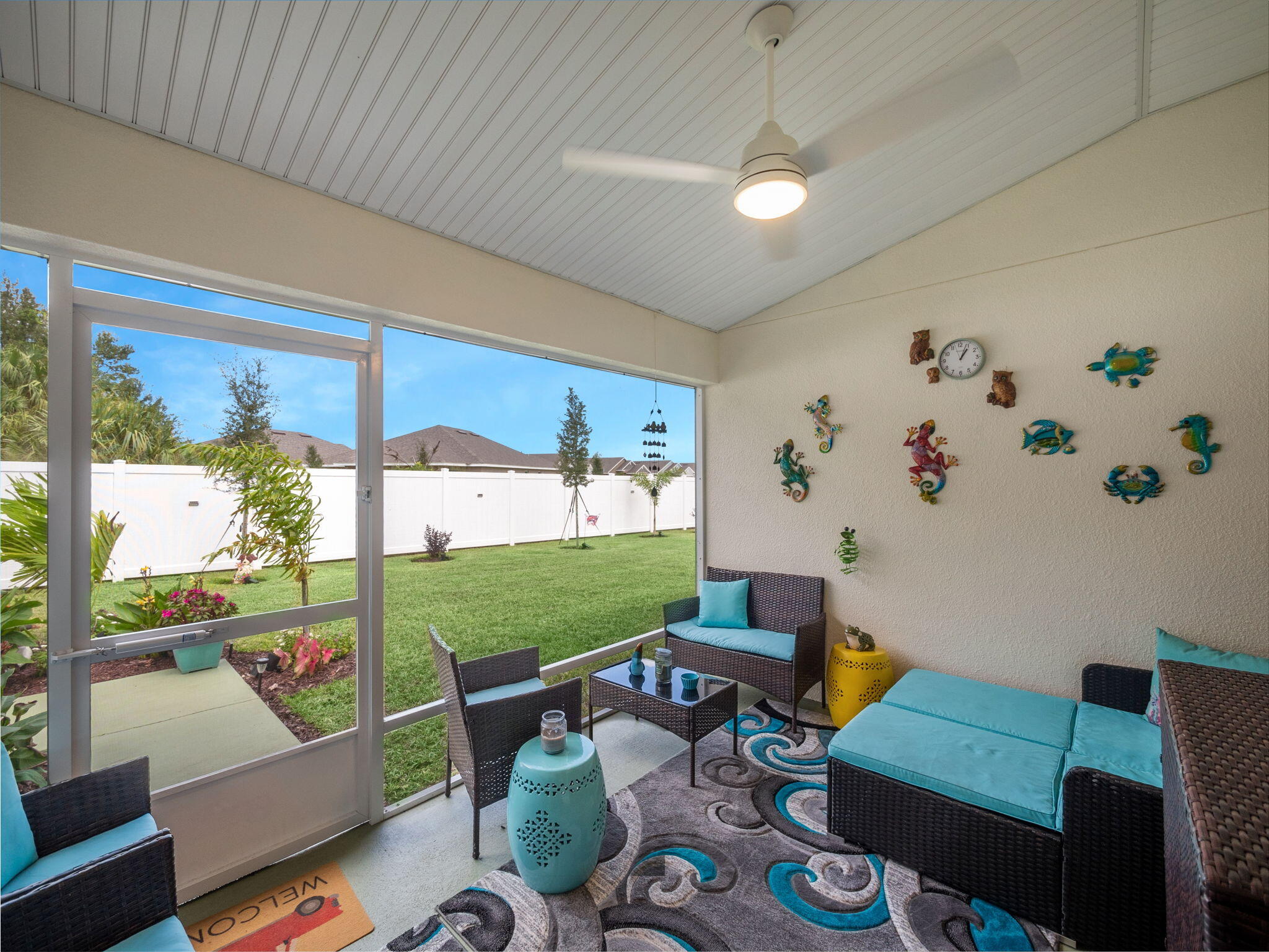 Screened-in patio with turquoise-cushioned wicker furniture, a ceiling fan, and views of the fenced backyard.