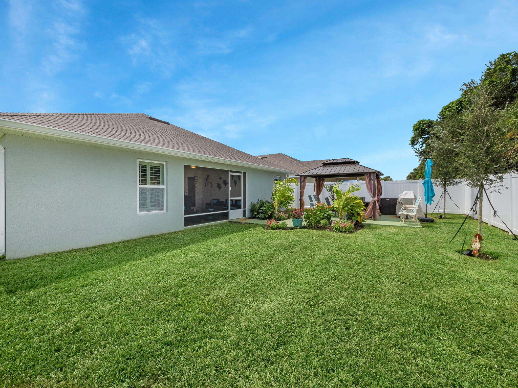 Home’s backyard with a broad lawn, white privacy fence, and curtained gazebo beside the patio.