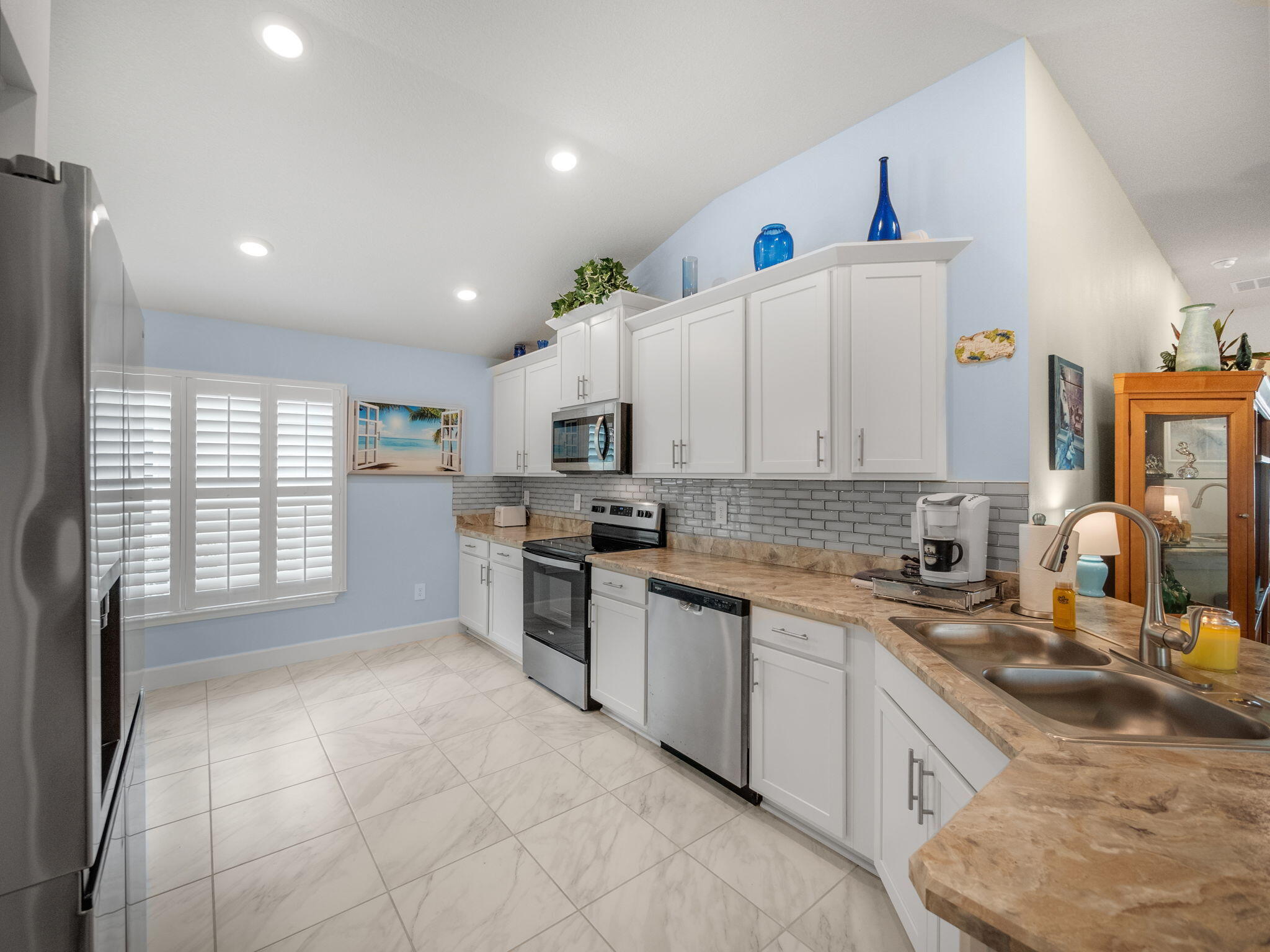 Kitchen with white cabinets, stainless appliances, stone counters, and plantation shutters.