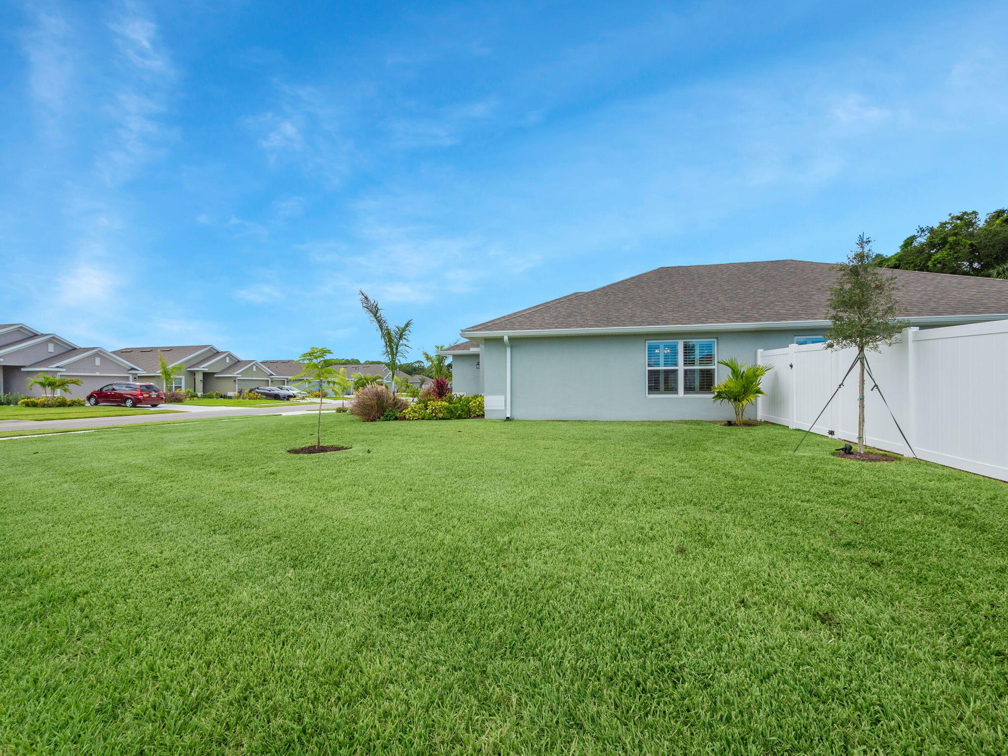 Side of a gray home beside a broad lawn and white privacy fence.