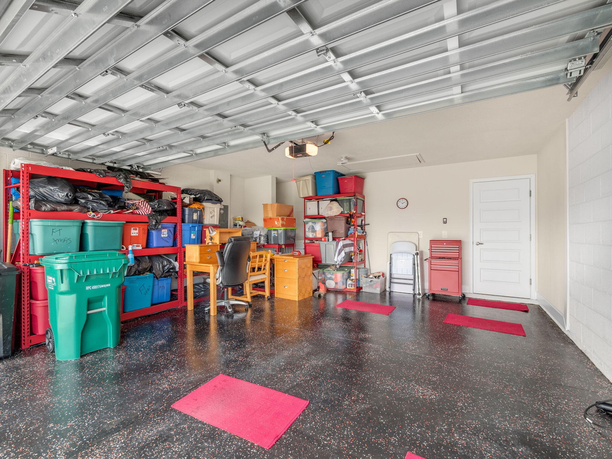 Garage with open overhead door, red storage shelves, a small desk, and a dark speckled floor.