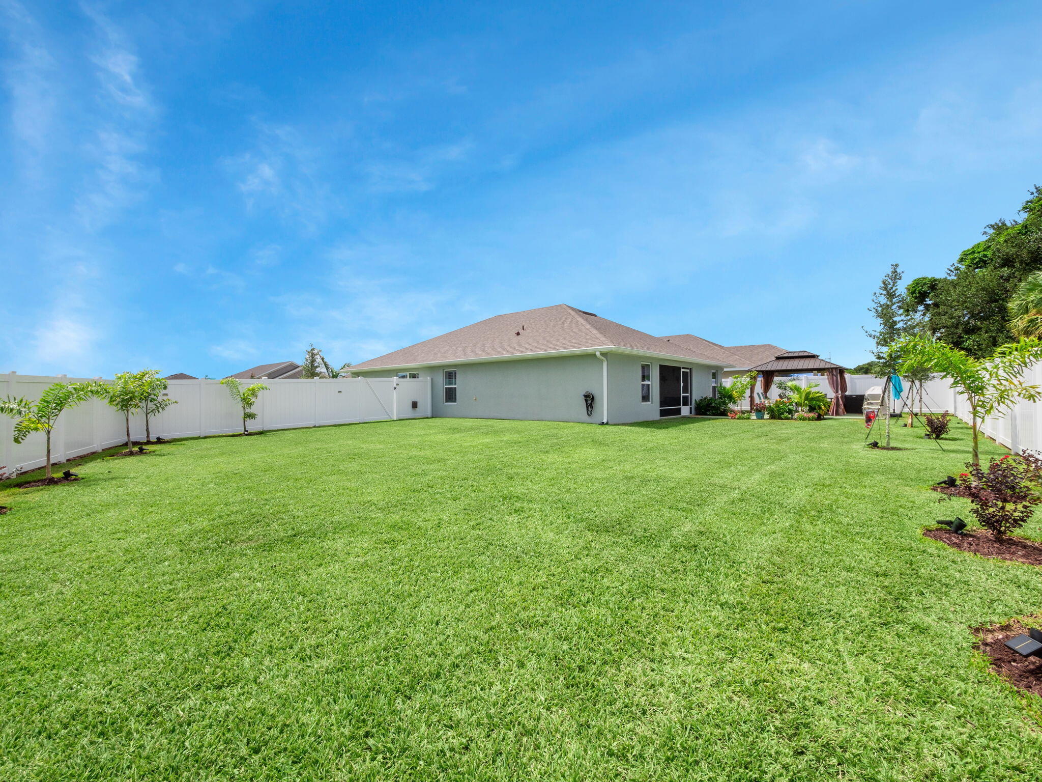 Fenced backyard with a wide lawn, white privacy fence, and gazebo beside the house.
