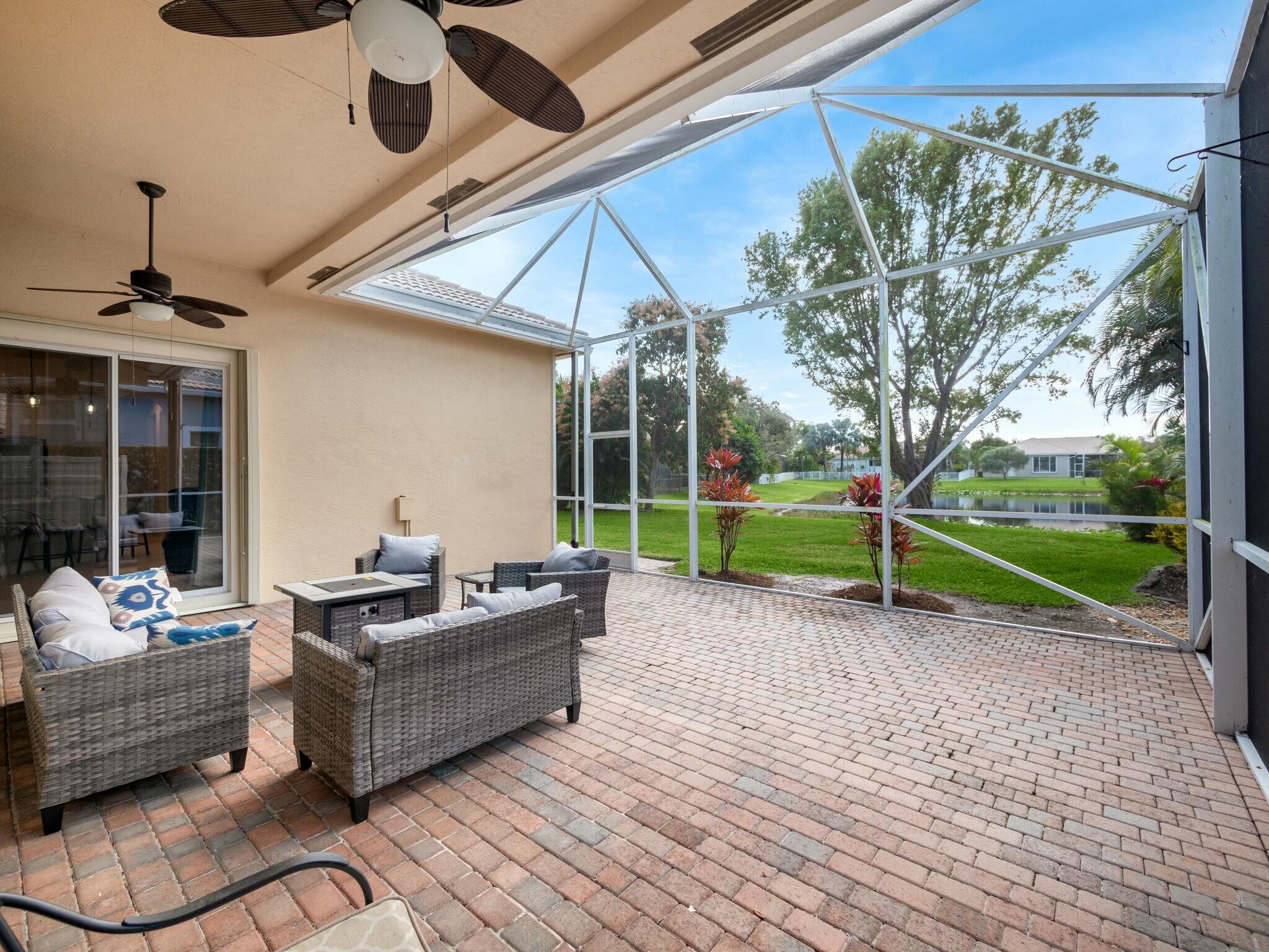 Screened patio with wicker seating and brick pavers overlooking a lawn and pond.