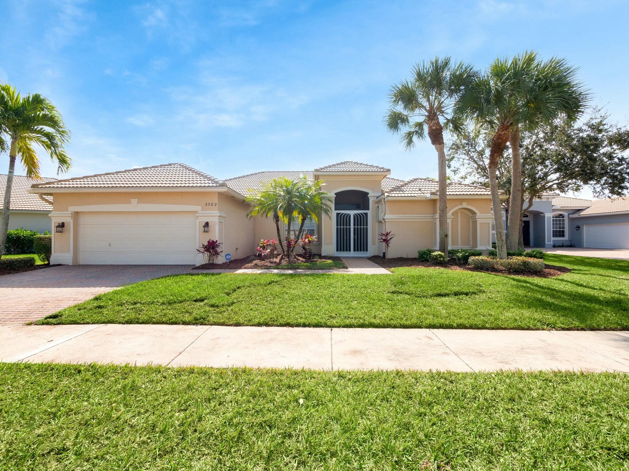 Tan stucco home with a tile roof, two-car garage, arched entry, and palm-lined lawn.