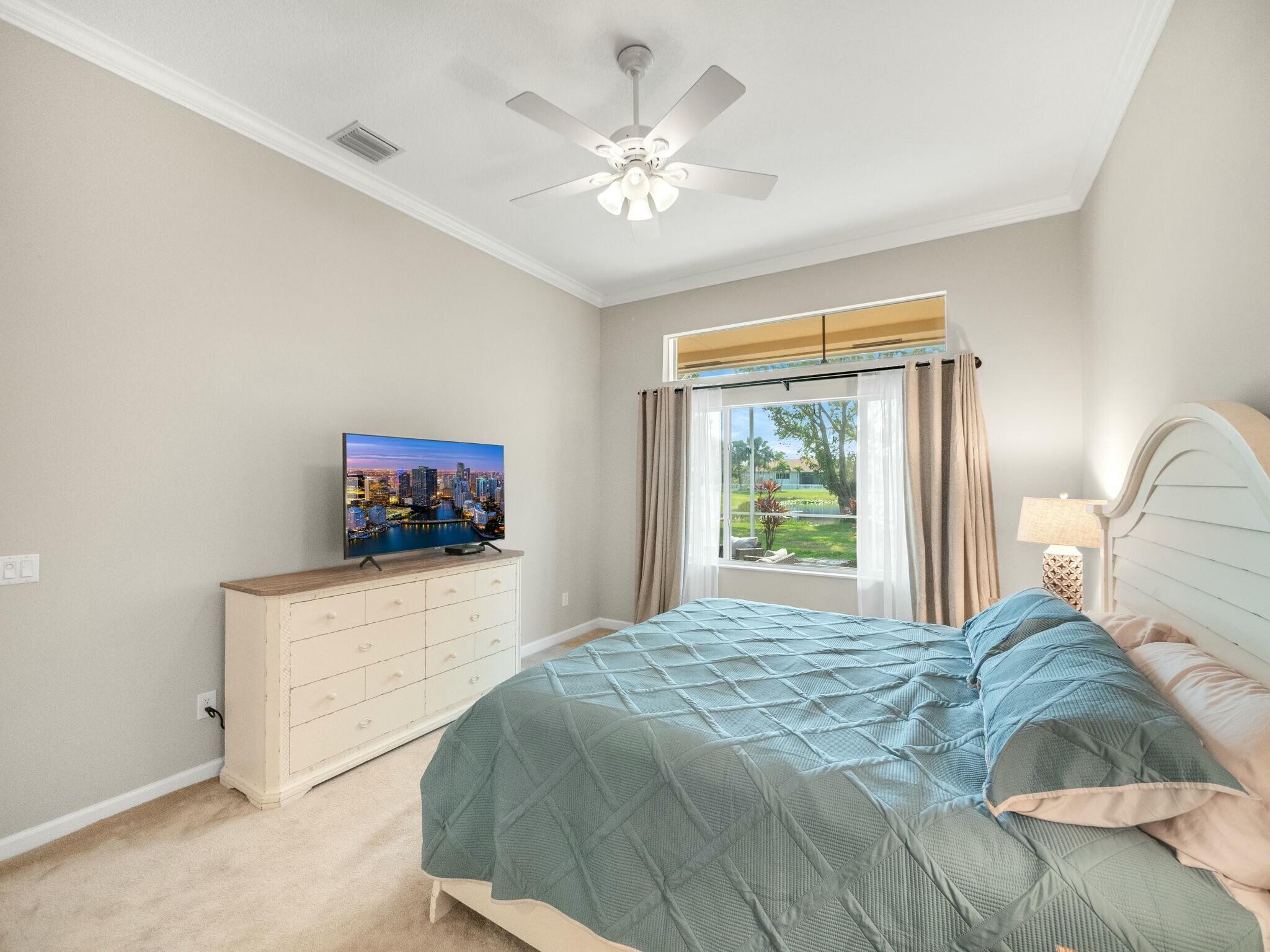 Bedroom with a blue quilted bed, white dresser, and window overlooking a green yard.