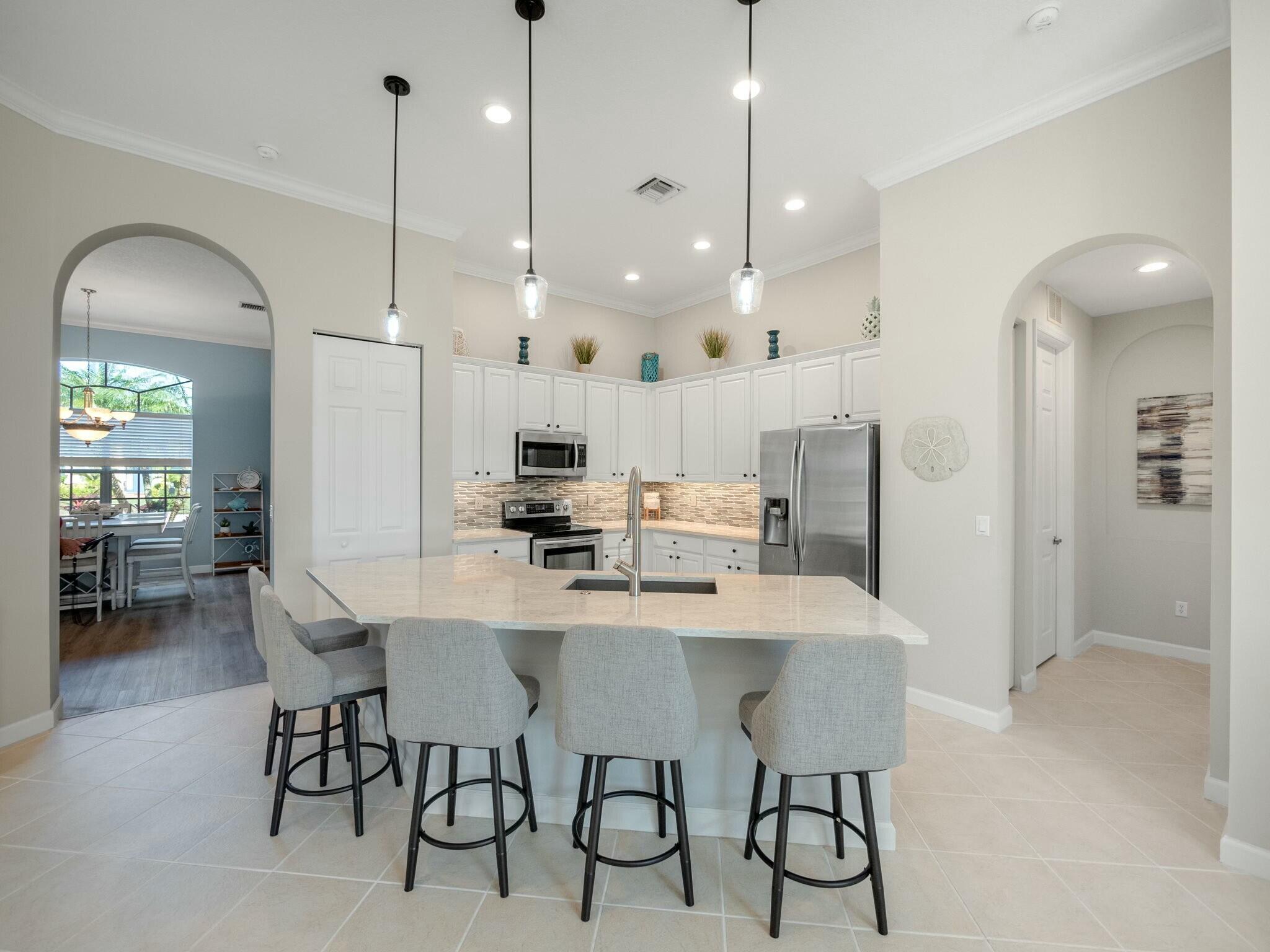 Kitchen with a large island, four stools, white cabinets, and stainless steel appliances.