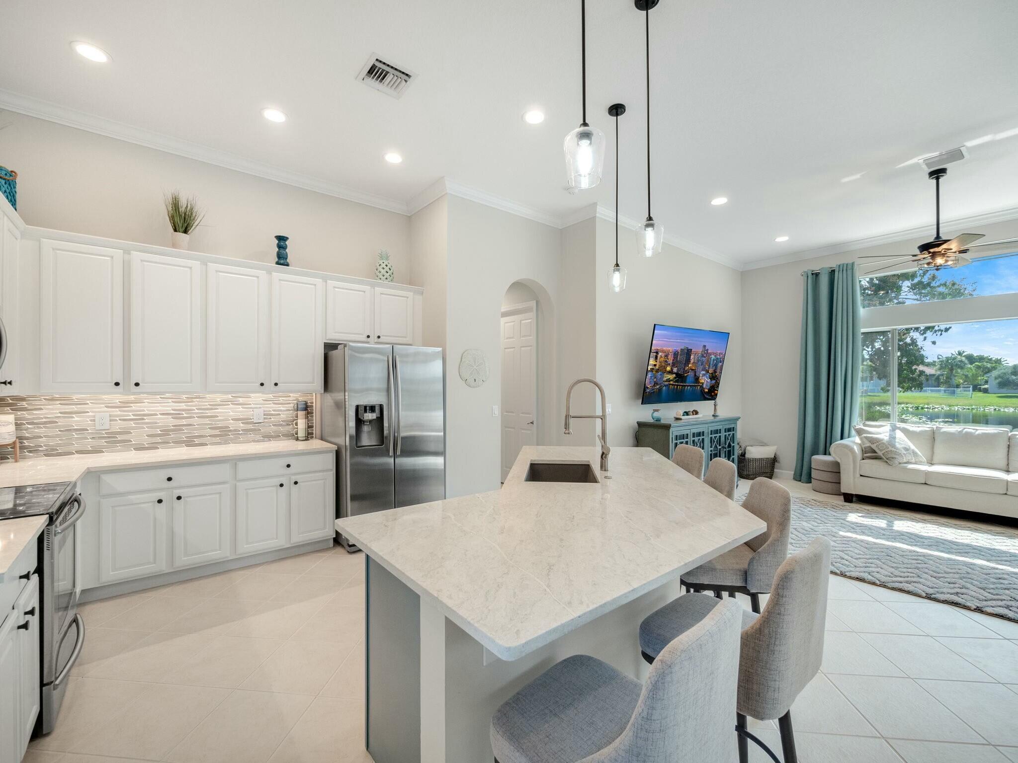 Open-plan kitchen with a large island, white cabinets, stainless steel appliances, and a living area overlooking water.