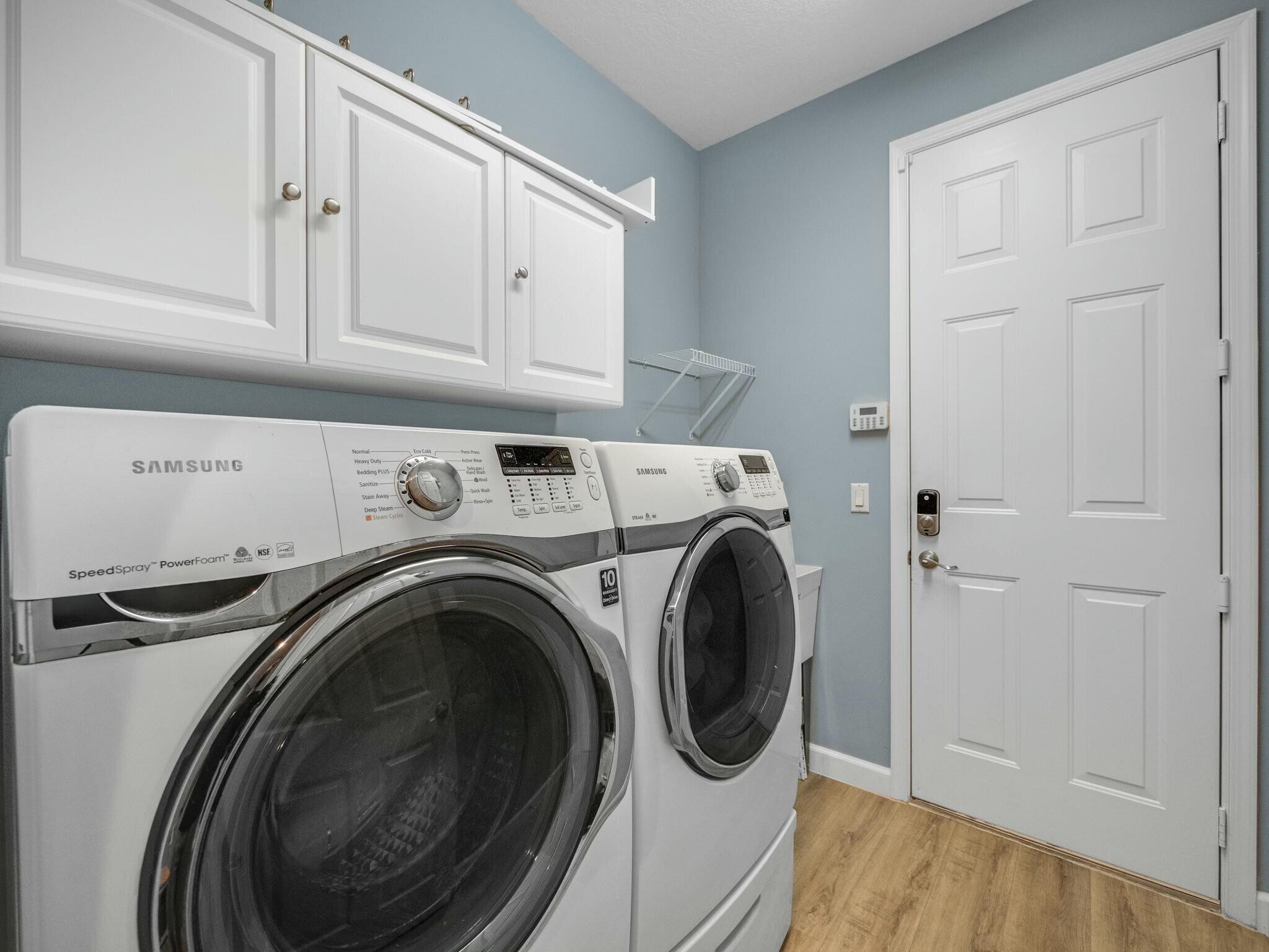Laundry room with Samsung washer and dryer beneath white cabinets.