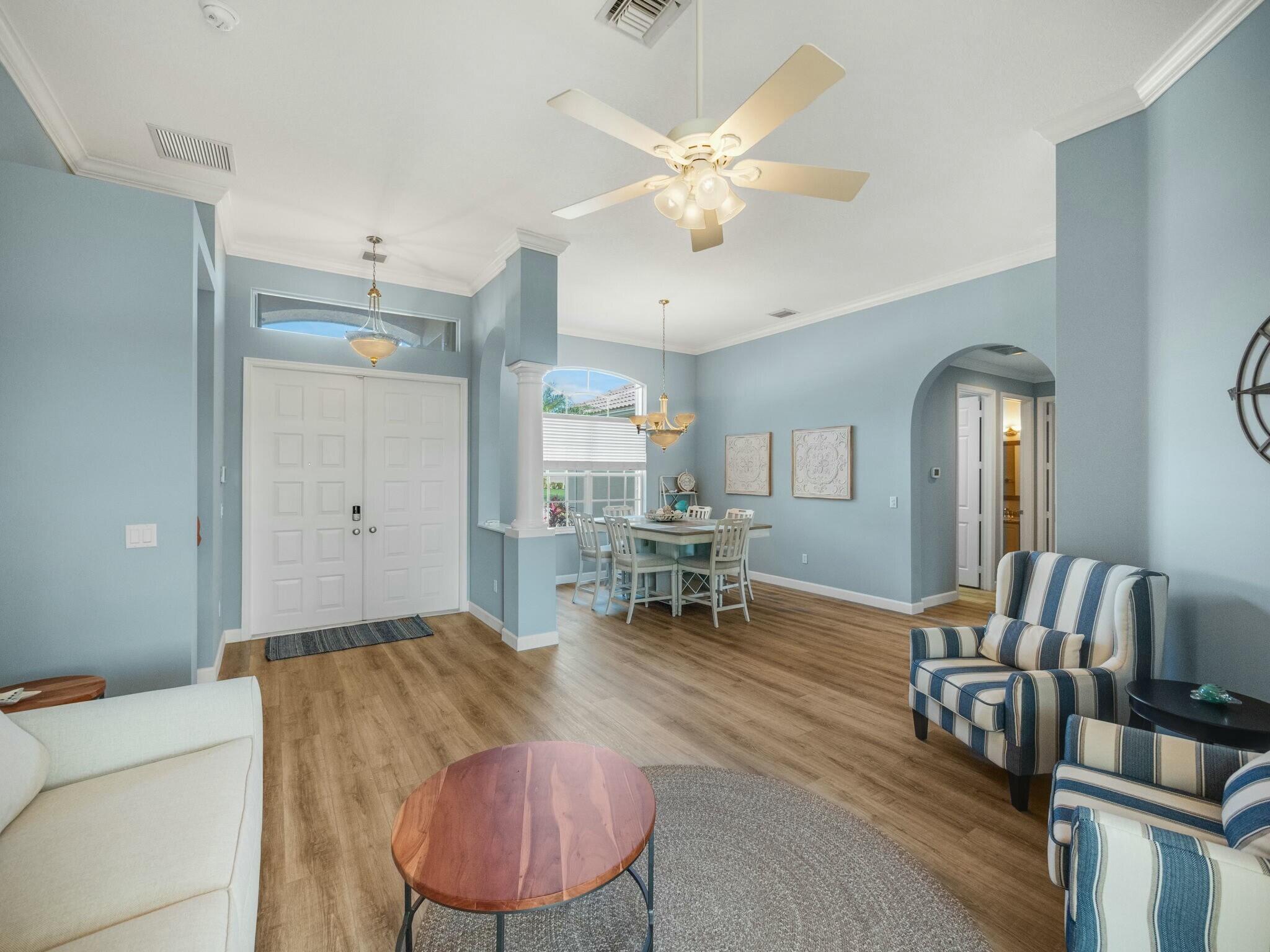 Open living and dining area with pale blue walls, wood-look floors, and striped armchairs.