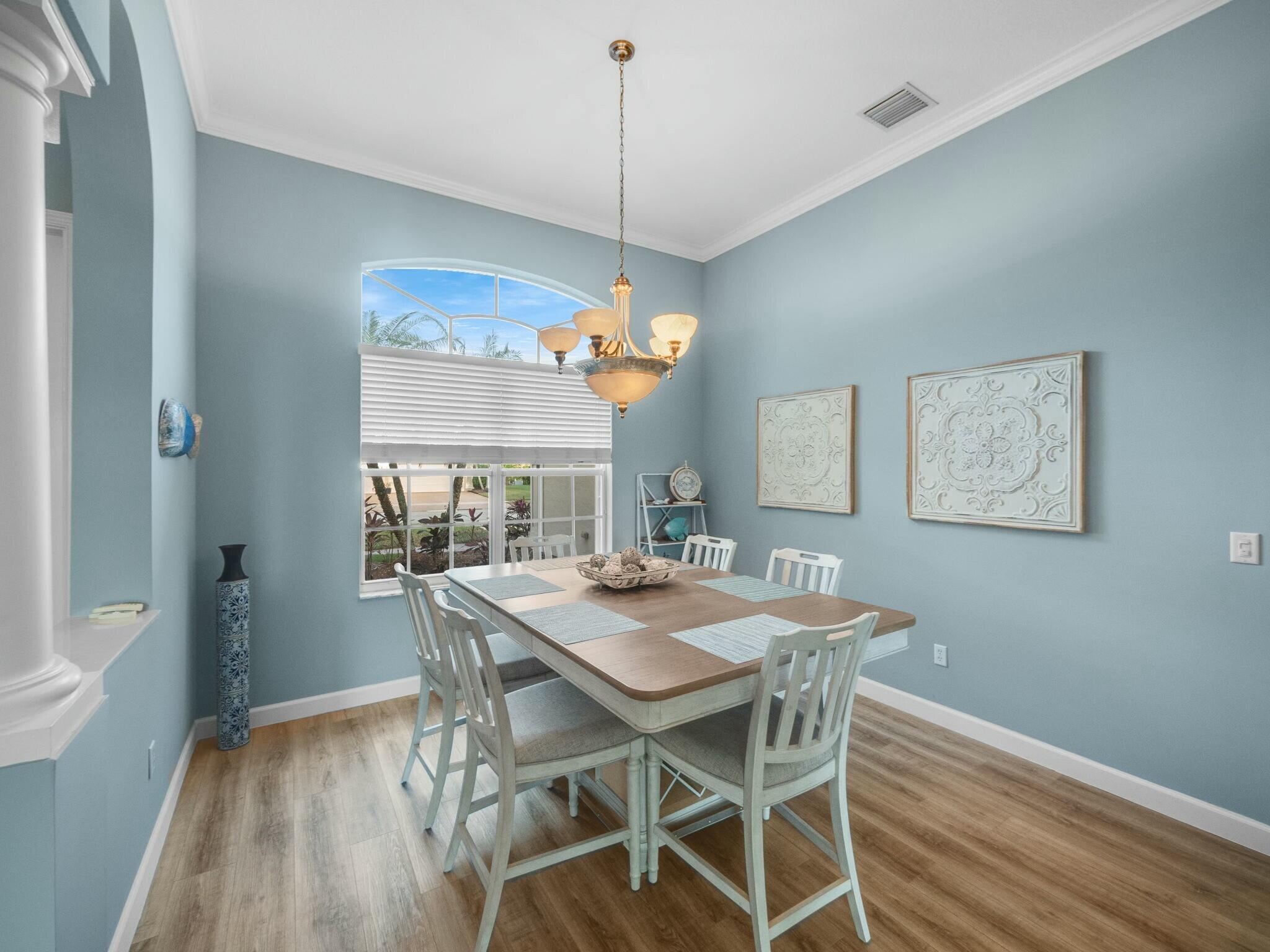 Furnished dining room with pale blue walls, a wood table, white chairs, and a large arched window.