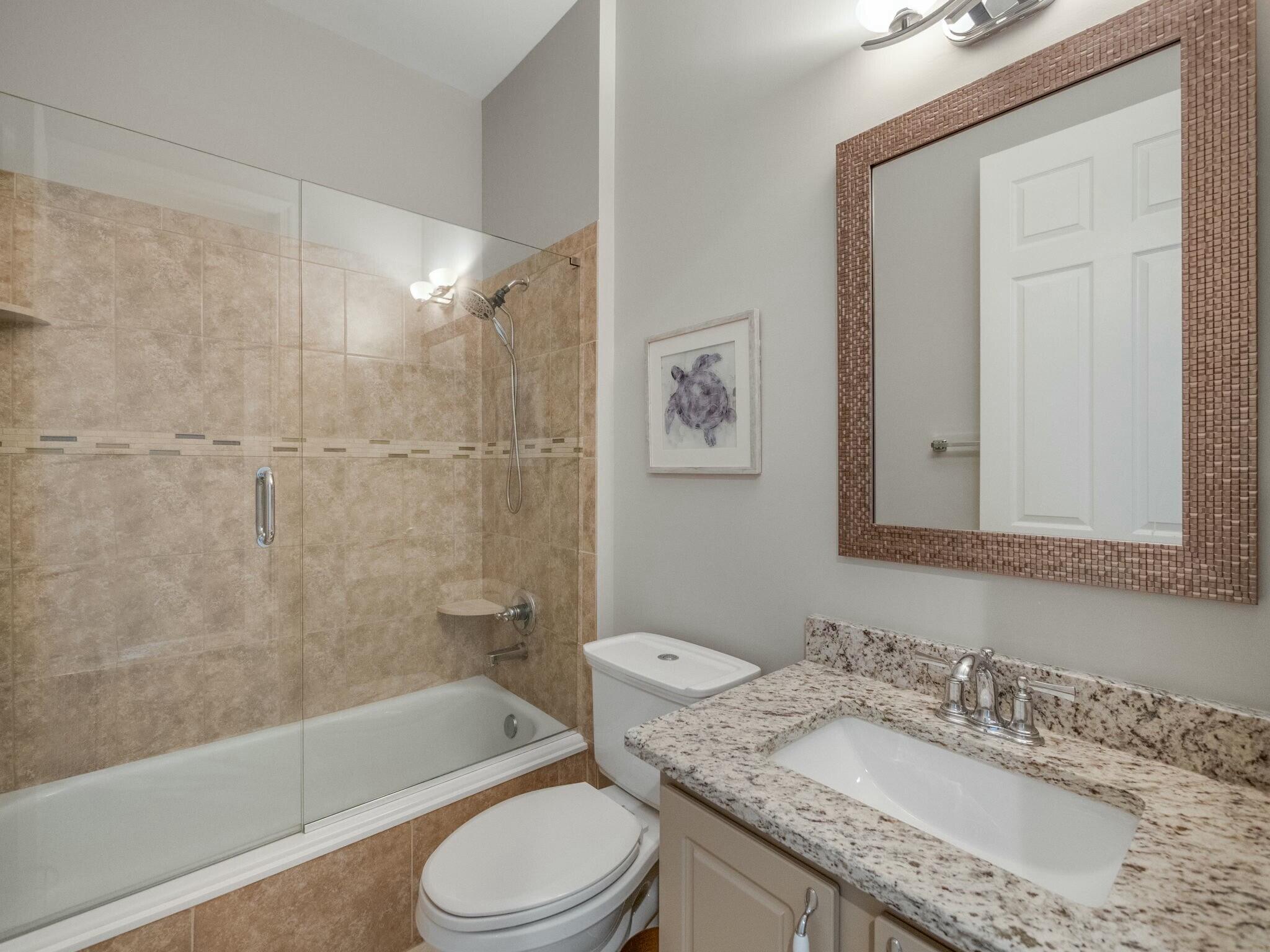 Bathroom with a glass-enclosed tiled tub and shower beside a granite vanity and large framed mirror.