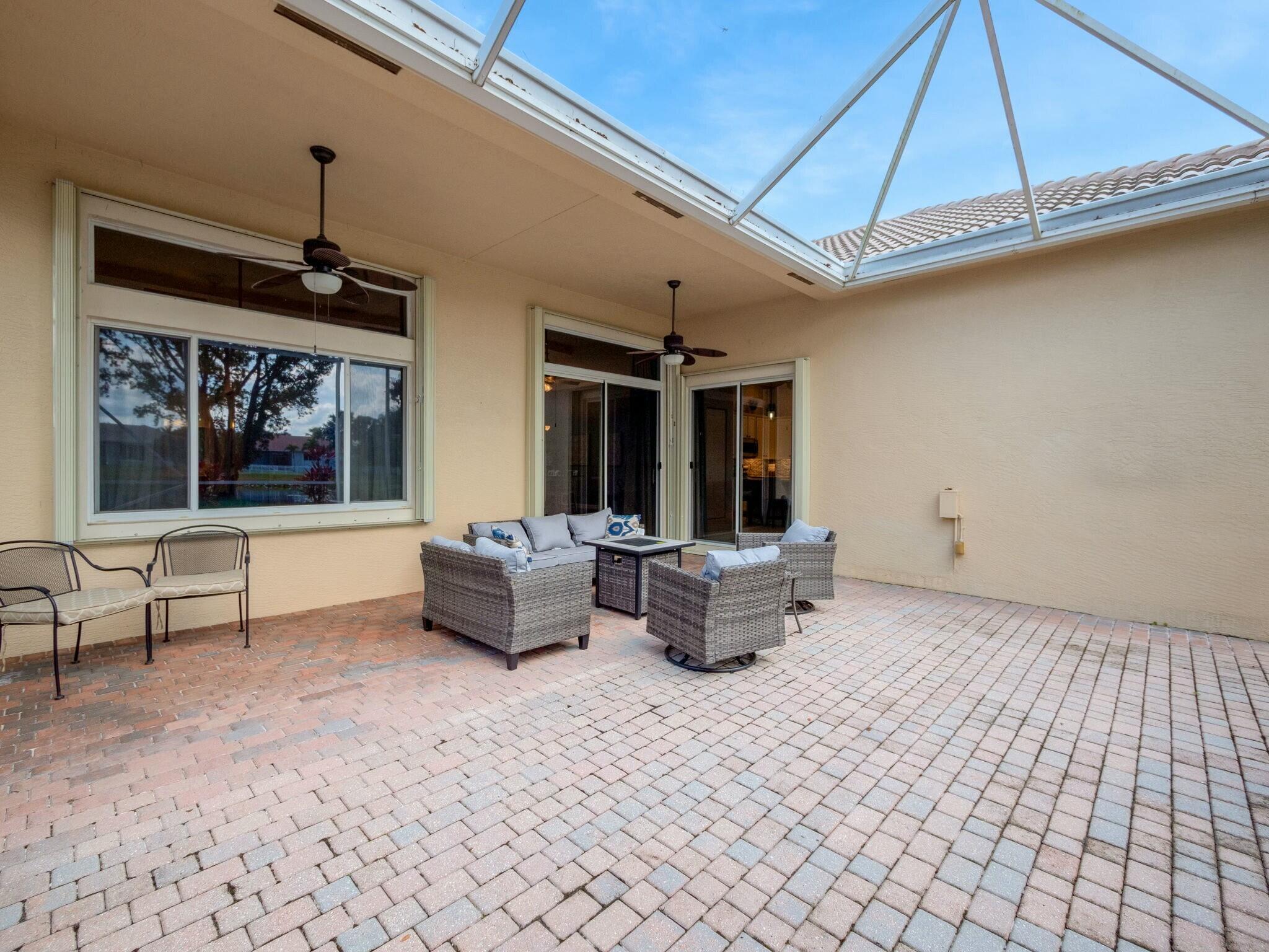 Covered patio with brick pavers, wicker seating, and a screened roof.