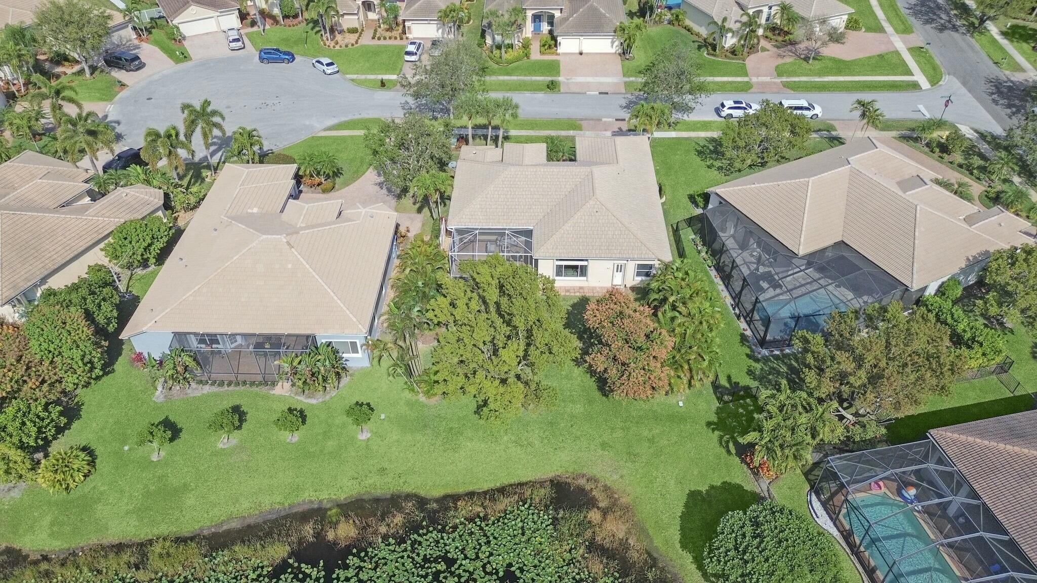 Aerial view of a home with a screened lanai, landscaped yard, and canal behind it.