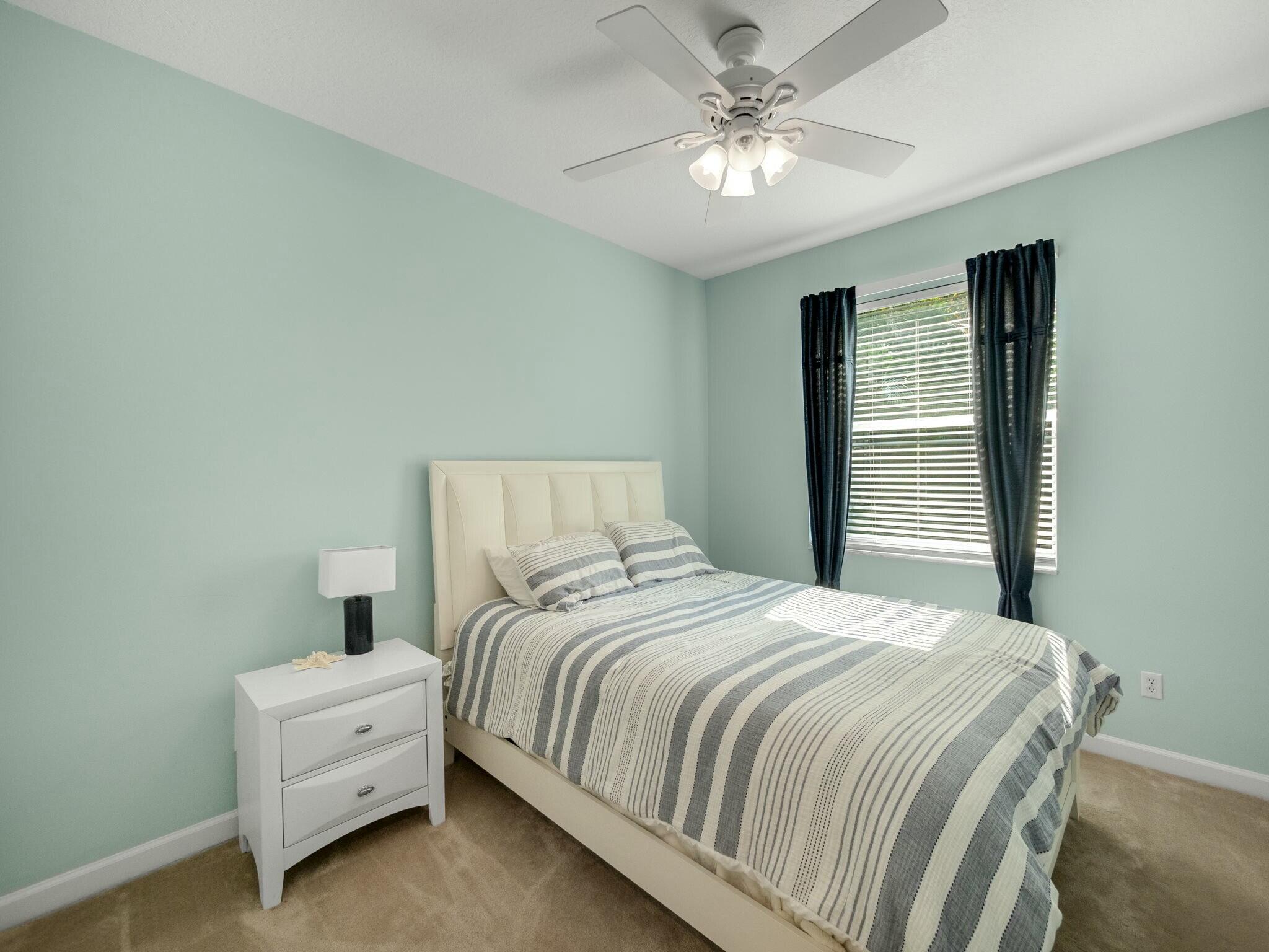 Furnished bedroom with mint-green walls, striped bedding, dark curtains, and a ceiling fan.